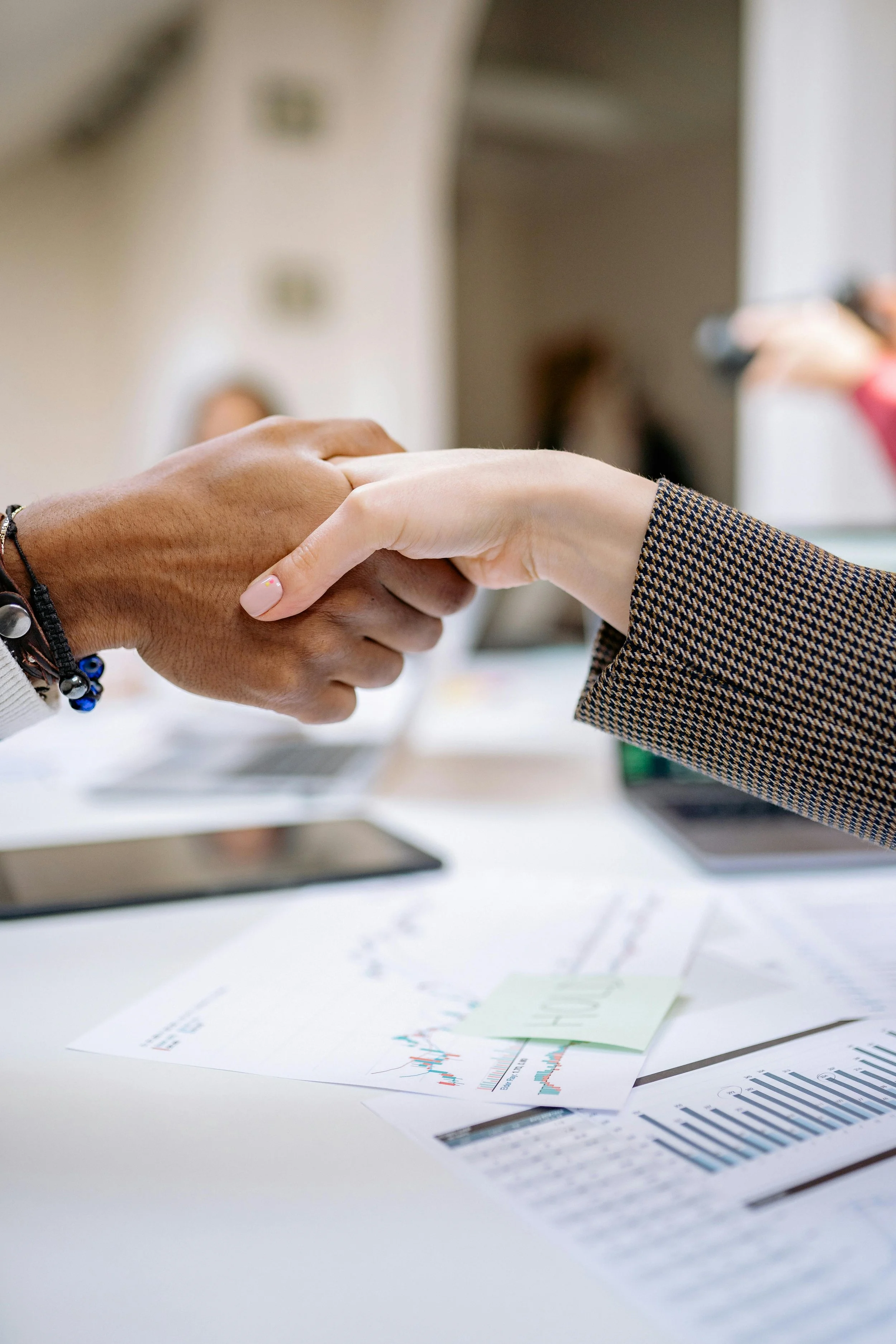 Two people shaking hands over a table with financial reports and charts.