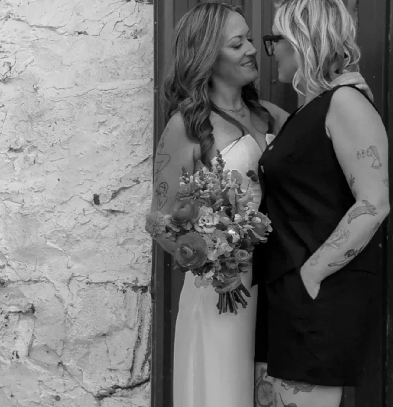 Two women looking at each other closely, holding flowers on their wedding day.
