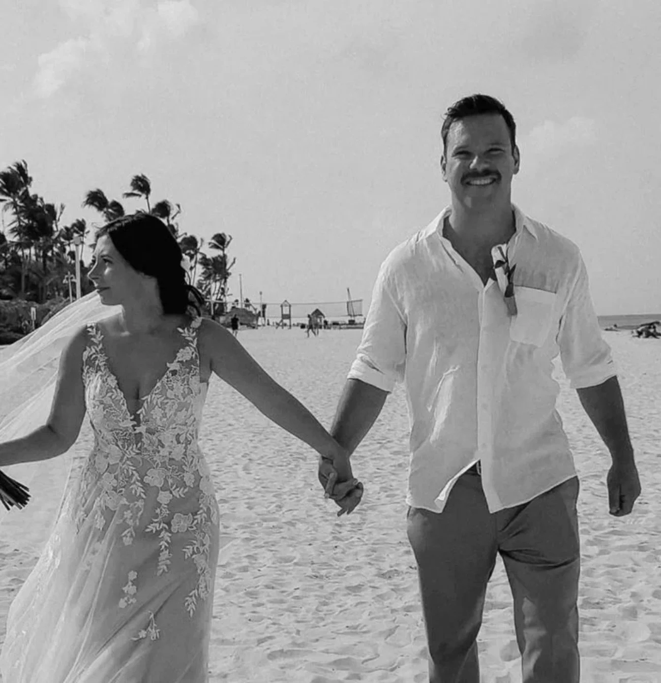 A newlywed couple holding hands on a beach.