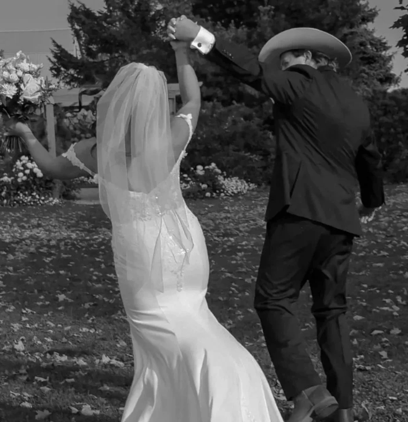 A bride in a wedding gown and veil dancing with a groom in a cowboy hat.