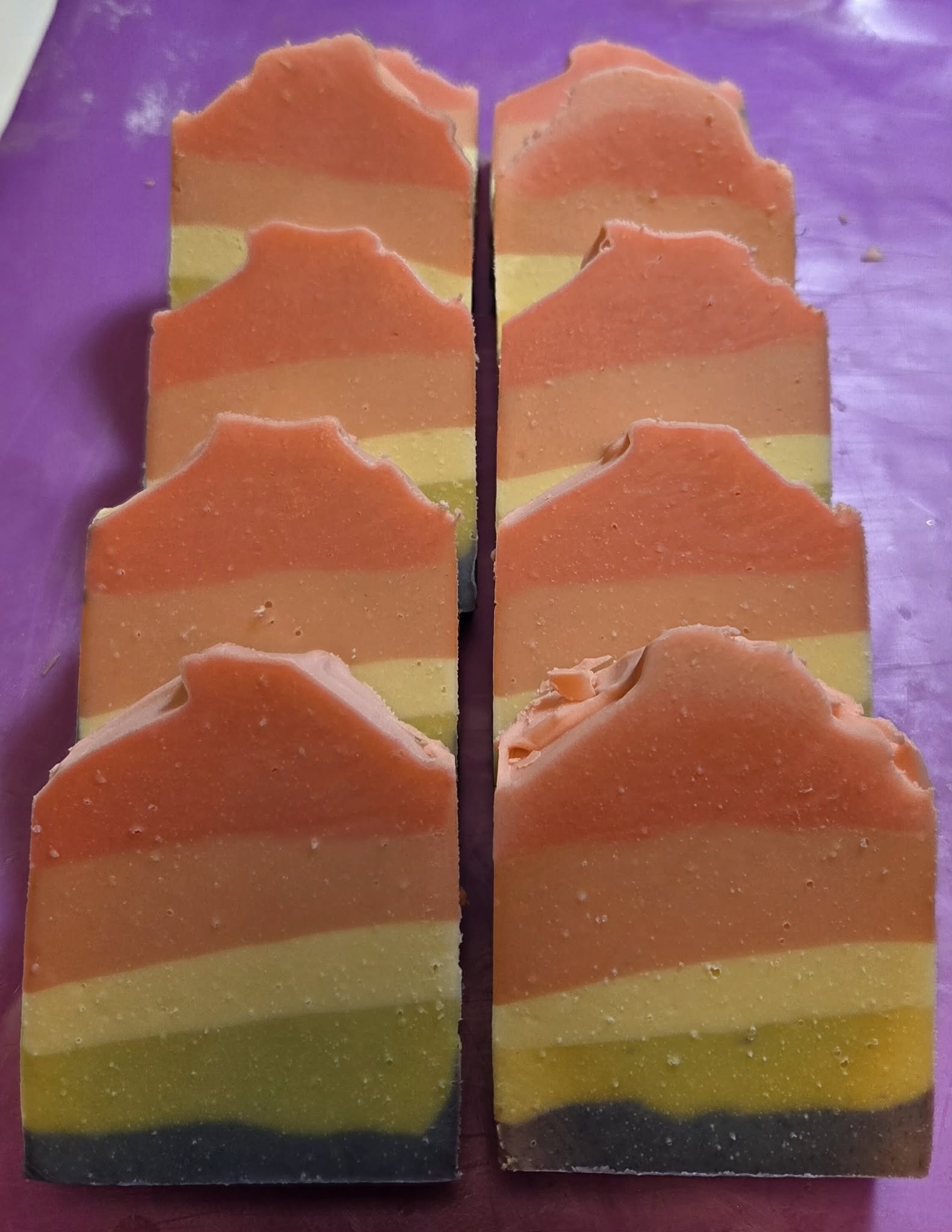 Colored soap bars with a layered design, featuring orange, pink, yellow, and black colors, on a purple surface.