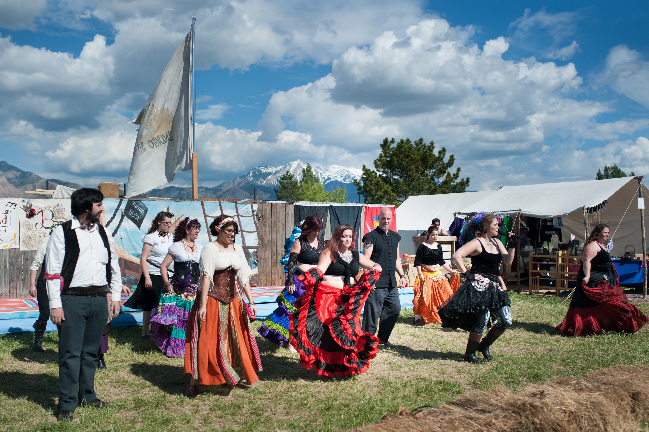People dancing in traditional folk costumes at an outdoor festival with tents and mountains in the background.