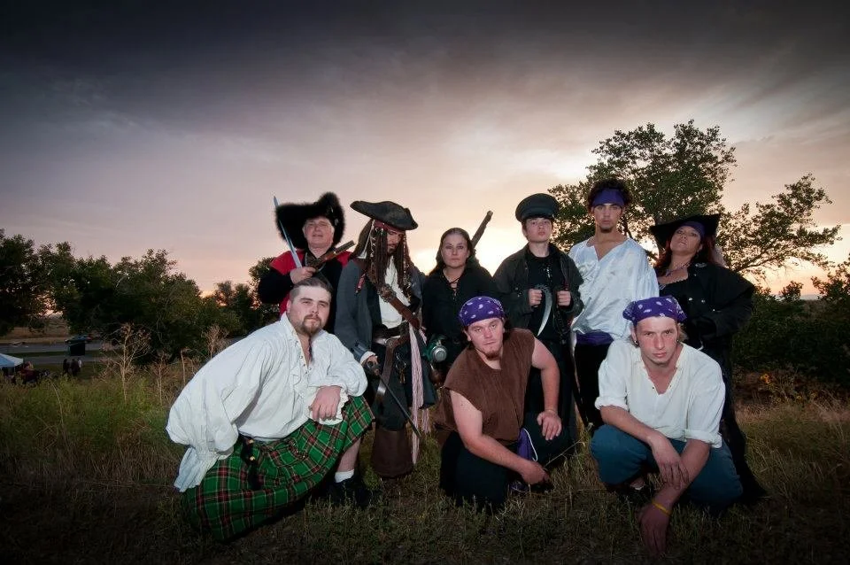 Group of people dressed as pirates outdoors at sunset.