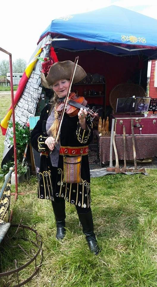 A woman dressed in a pirate costume playing a violin at an outdoor event.