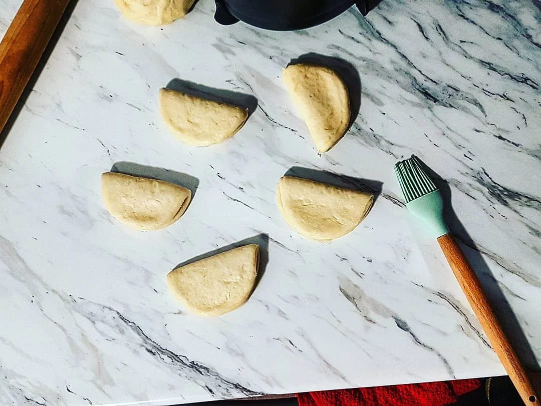 Five semi-circular pieces of boa bun dough on a marble countertop, lightly oiled and ready to be steamed for pork belly boas.