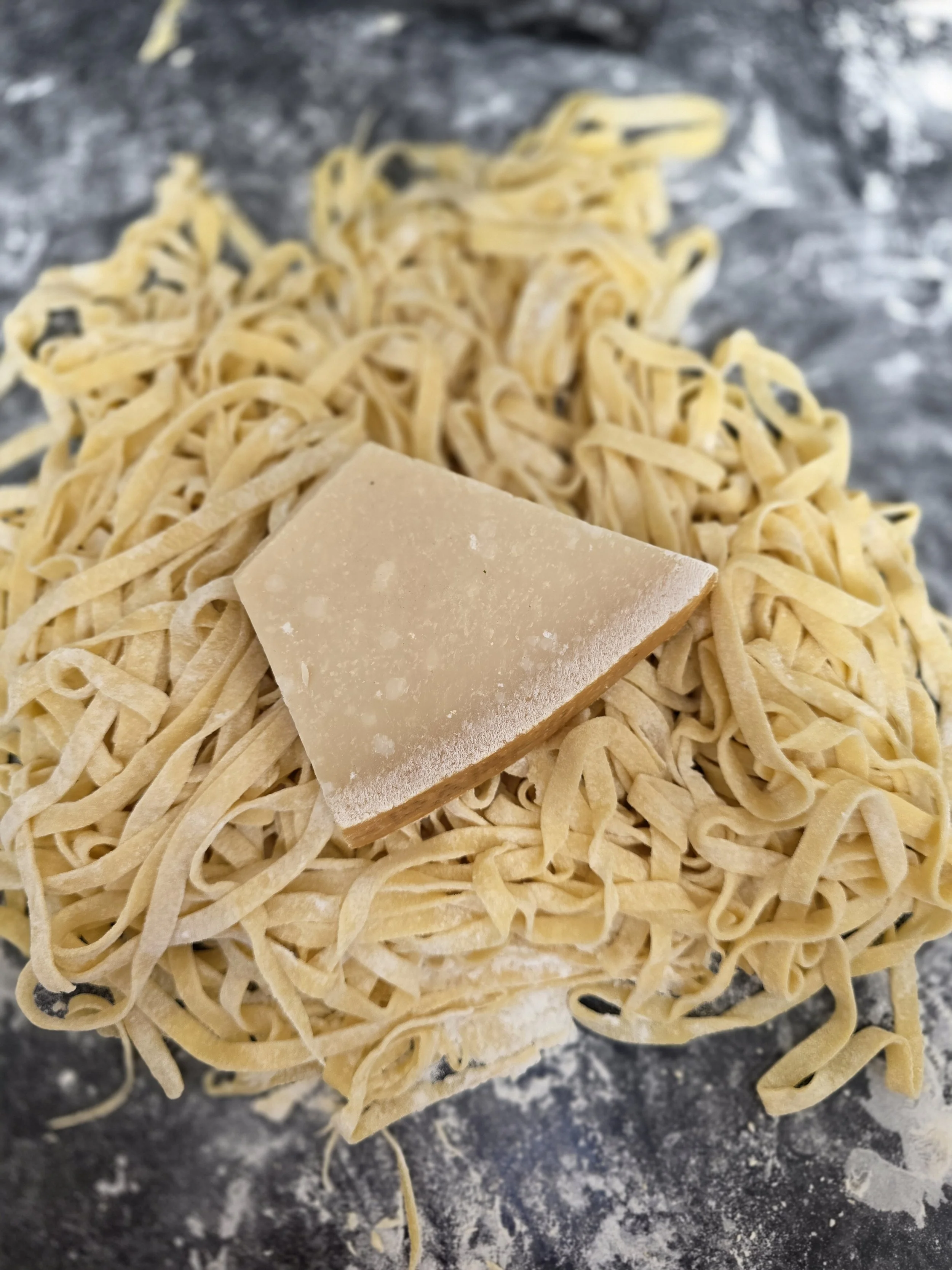 Freshly hand made pasta nest with a piece of parmiggiano reggiano cheese on top, on a floured surface.