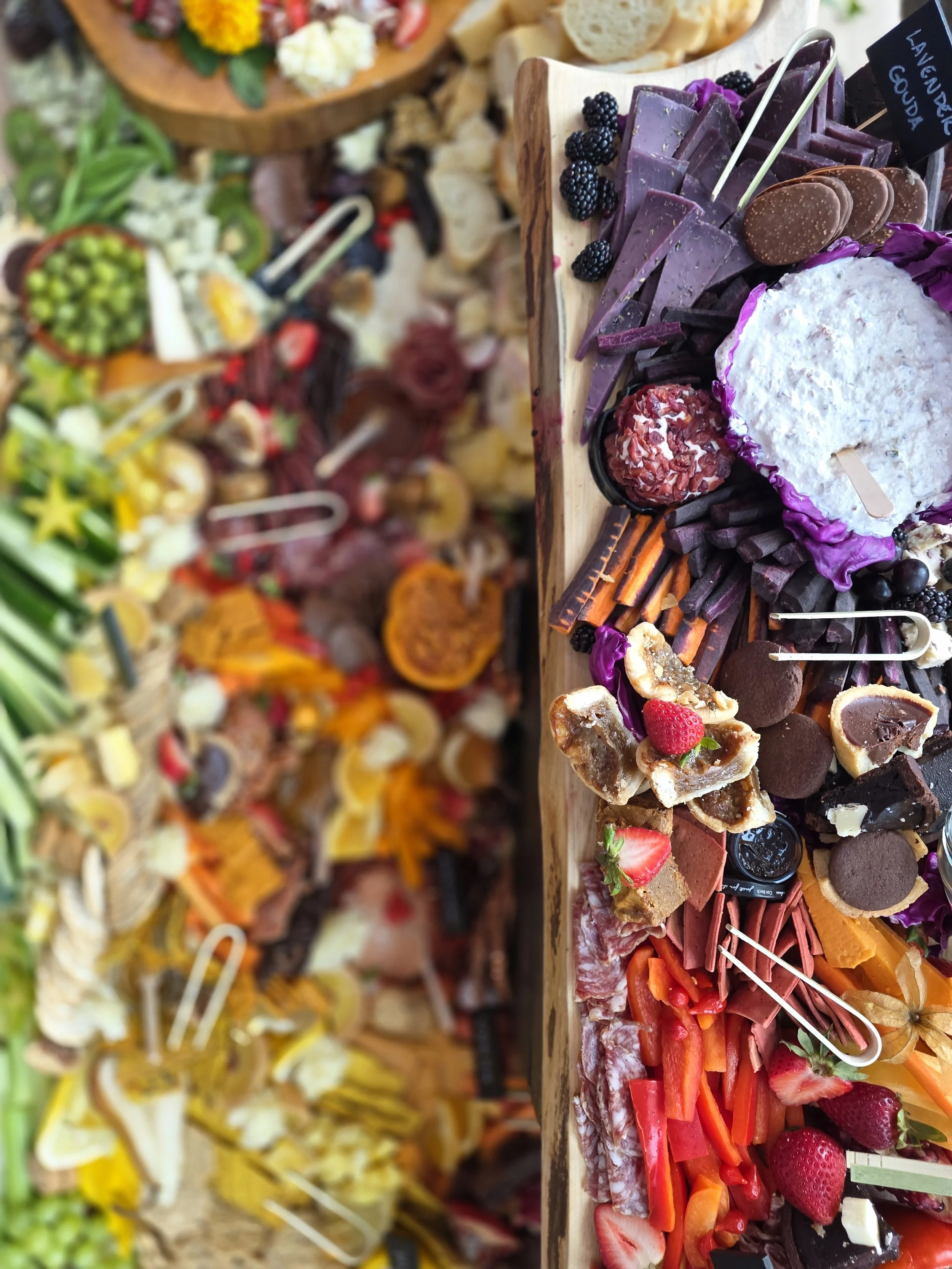 Assorted desserts on a wooden platter including chocolates, strawberries, berries, and various confections, part of a larger spread of food and sweets. Events, wedding spreads, colourful food, buffet inspiration