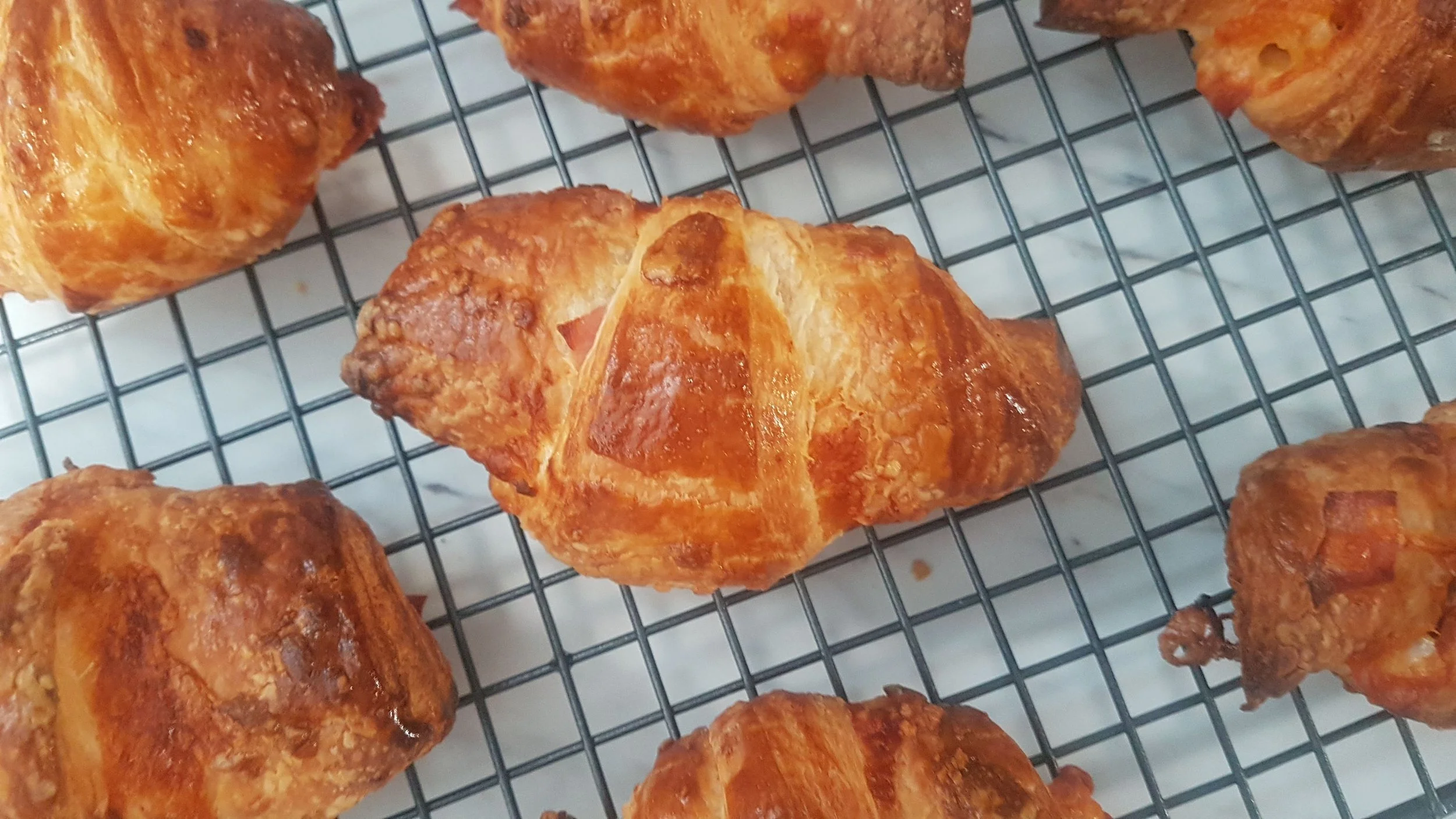 Golden-brown flakey croissants cooling on a wire rack. Home made from scratch