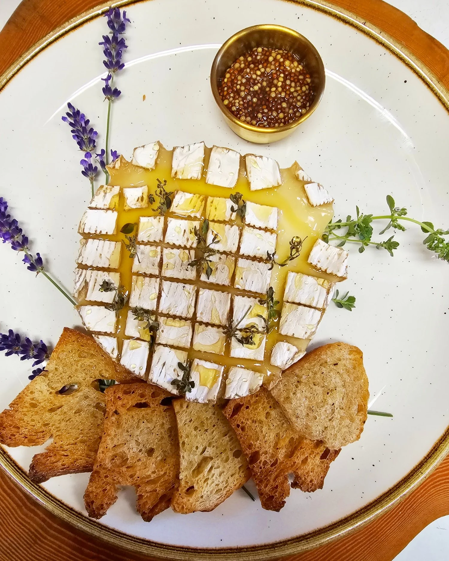 Beautifully presents wheel of brie, drizzled in honey and served with toast and dijon mustard garnished with thyme and lavender. Cheese pairings and small plate ideas.
