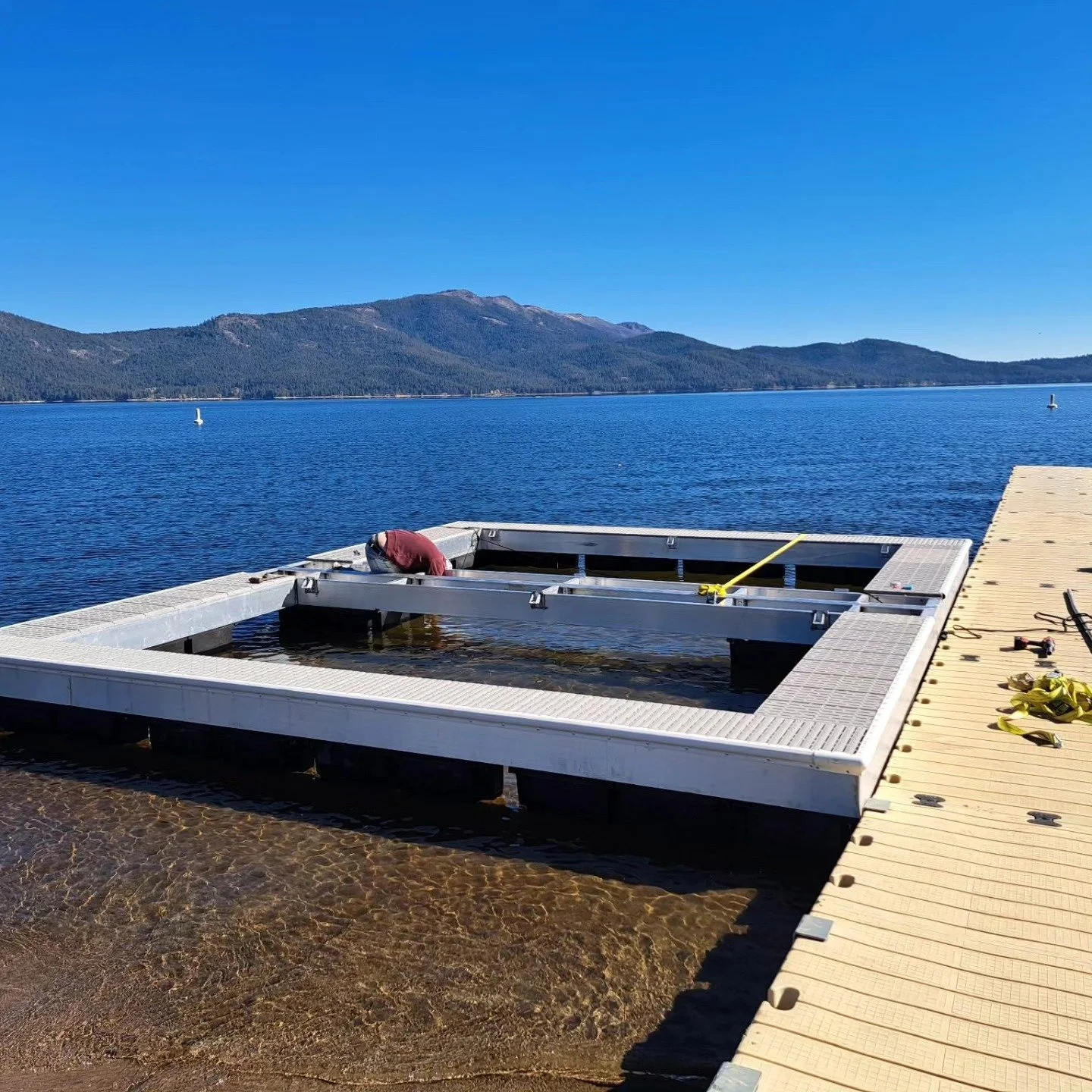 A floating dock under construction on a lake with mountains in the background, tools and equipment on the dock, and calm blue water.