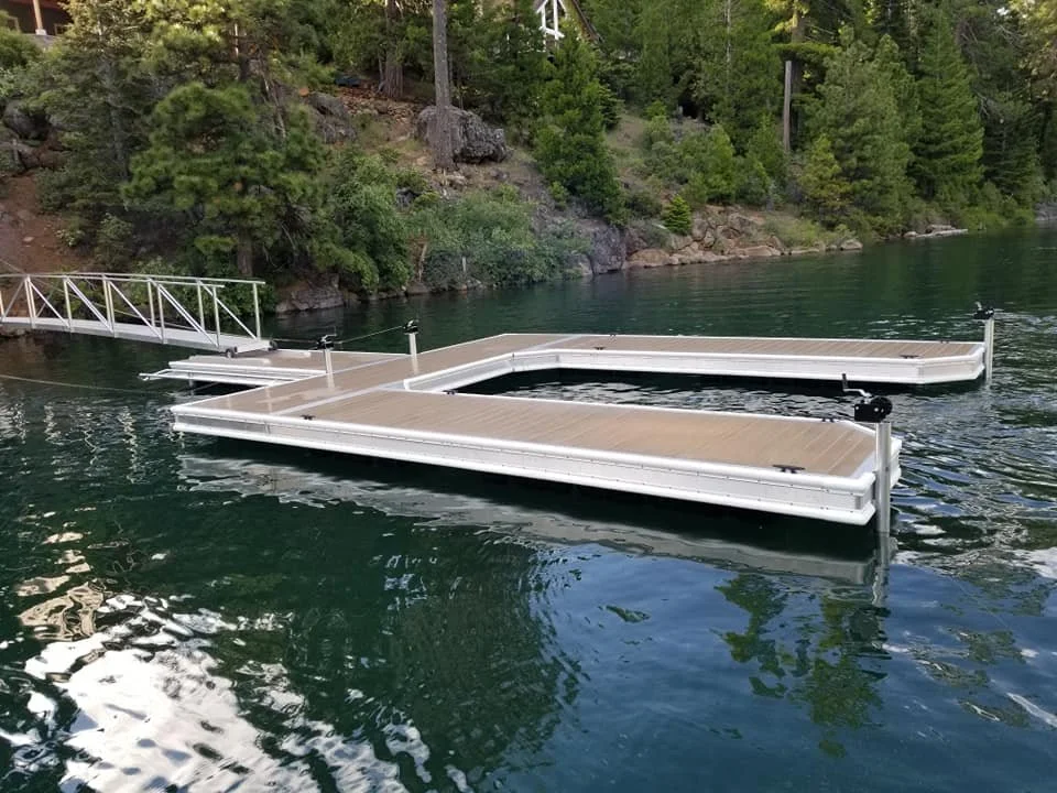 Floating dock with a ramp on a body of water, surrounded by trees and rocky shoreline.