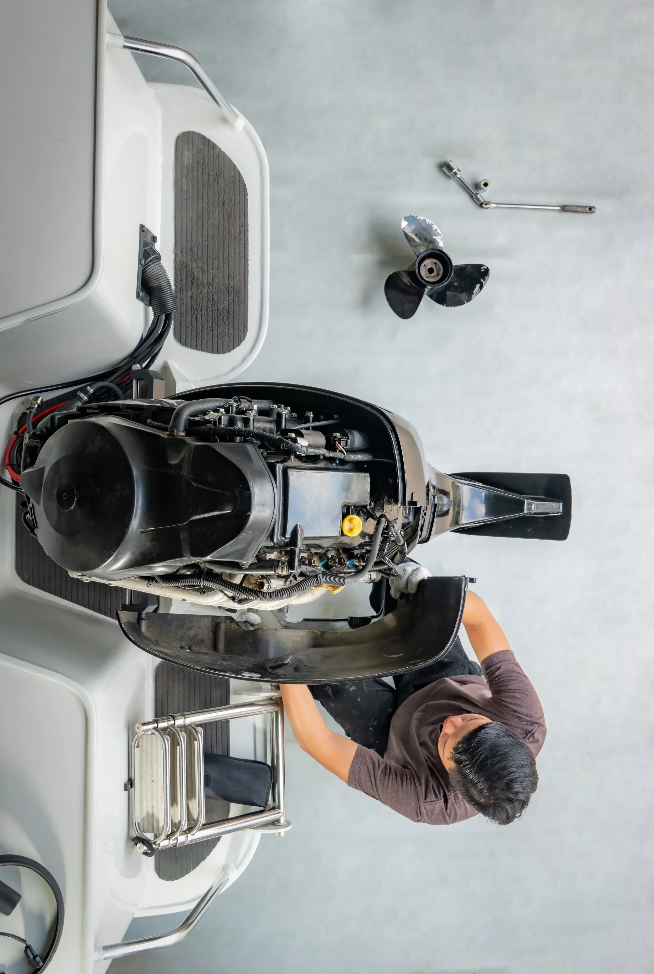 A person working on the outboard motor of a small boat in an indoor setting, with a propeller and various tools on the table.