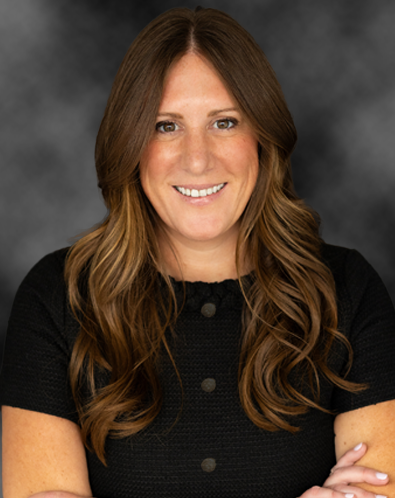 Portrait of a woman with long, wavy brown hair, smiling, wearing a black top, against a dark studio background.