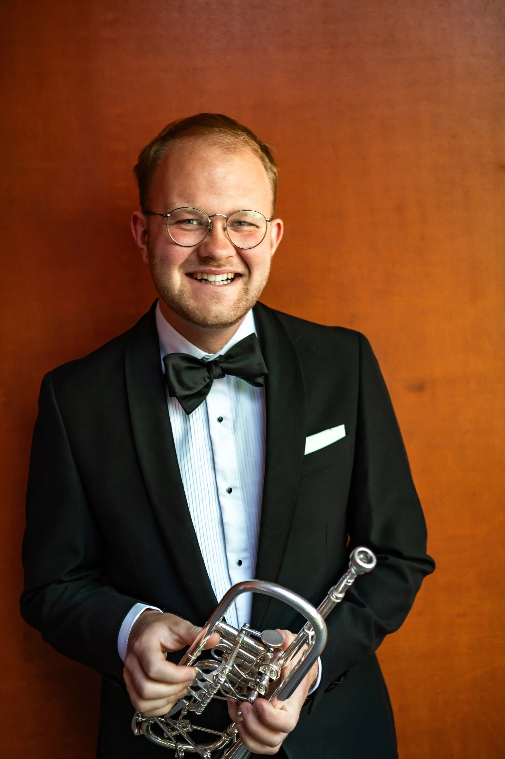 A smiling young man in a tuxedo holding a trumpet.