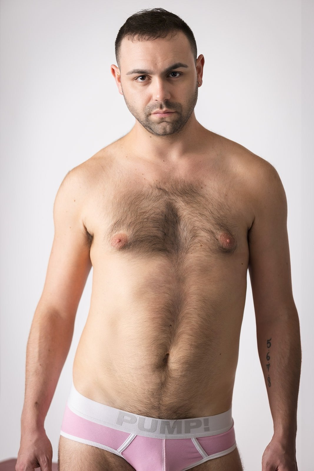 A shirtless man in pink underwear with the word "PUMP!" on the waistband, standing against a plain background.