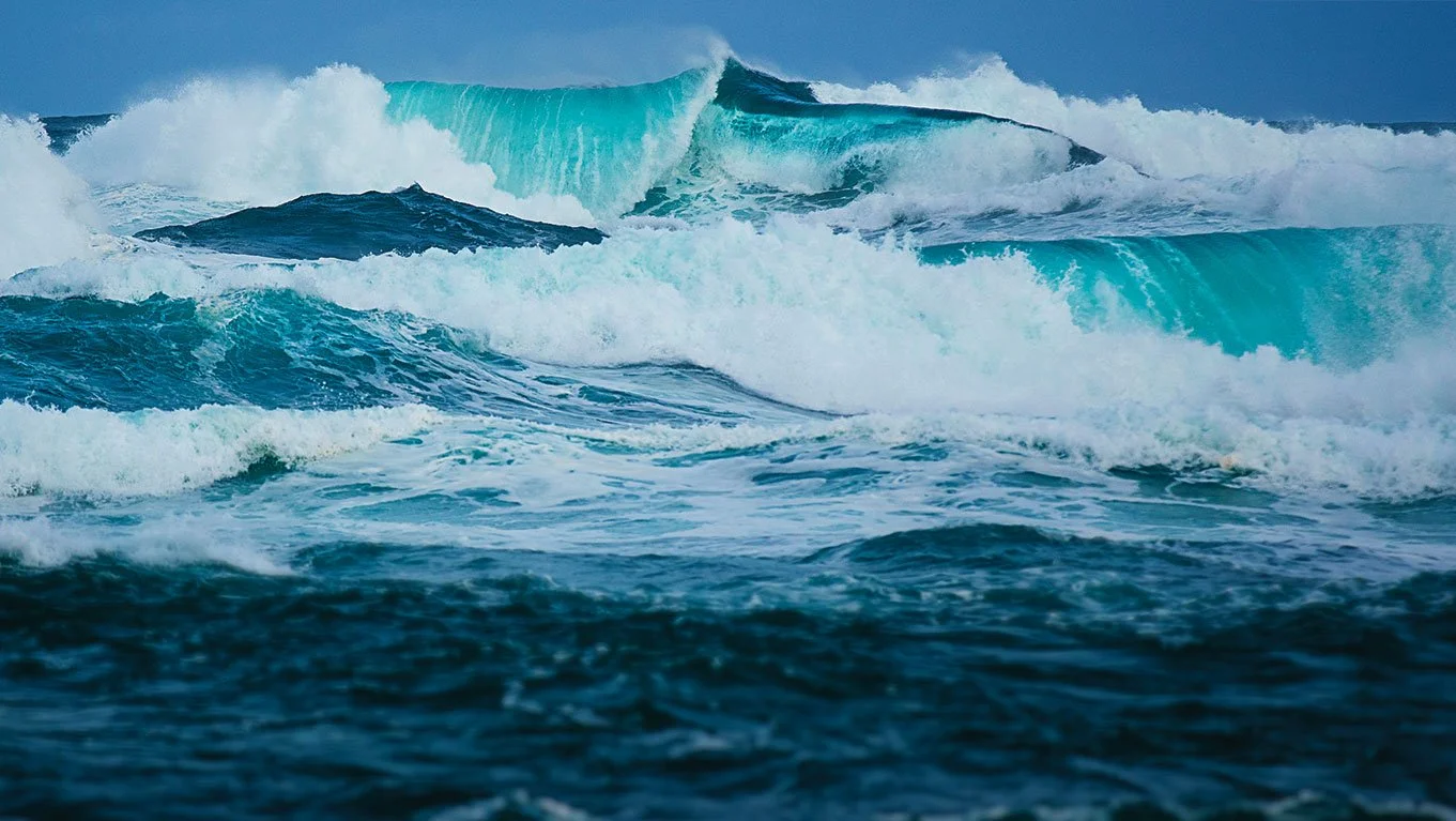 Ocean waves crashing with large waves in the background and swirling water in the foreground.
