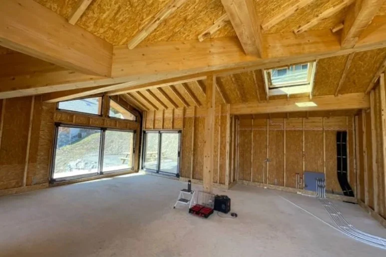 Interior of a new build eco house under construction with exposed wooden framing, large windows, and skylight.