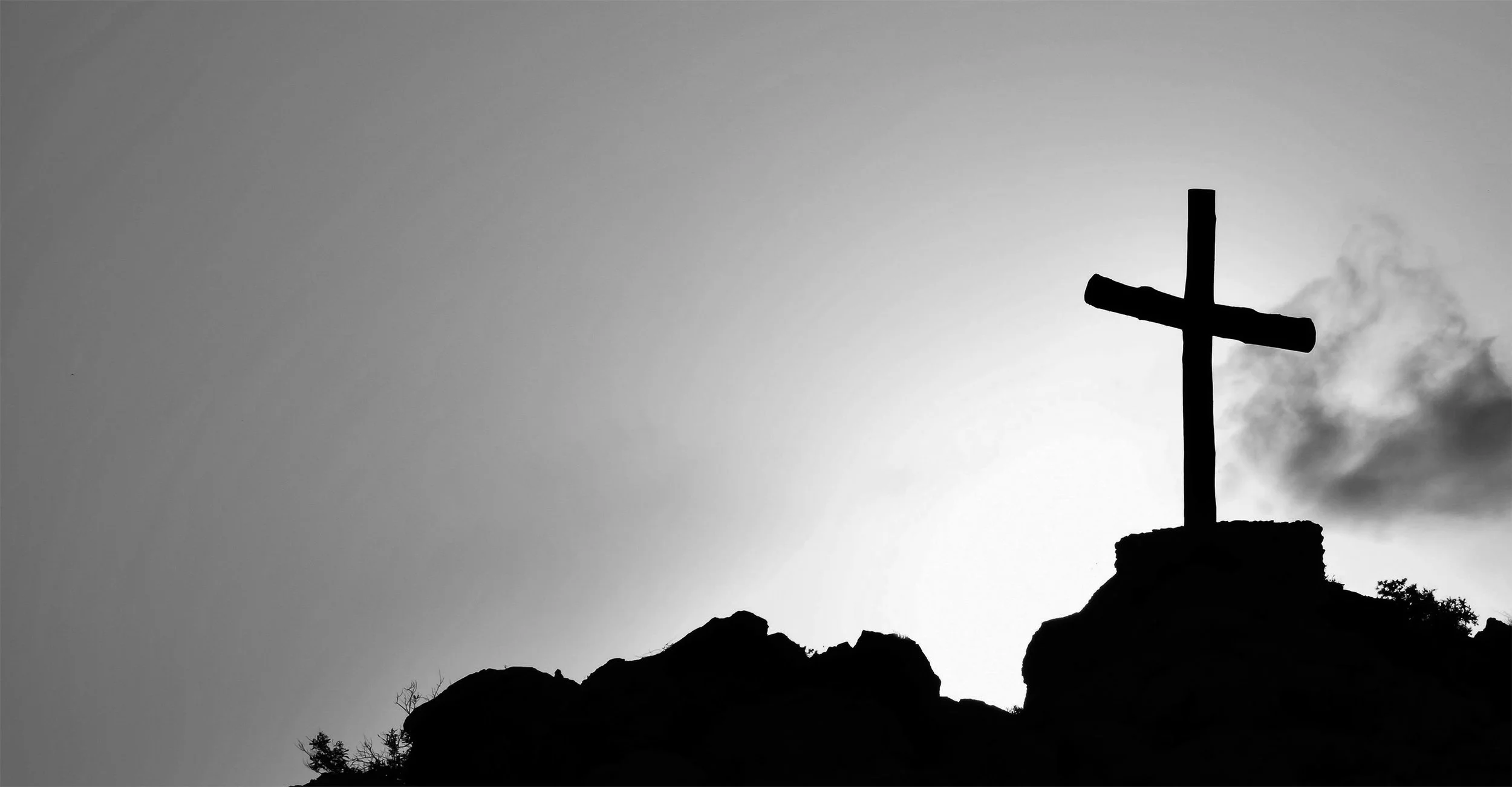 A silhouette of a Christian cross standing on a rocky hilltop against the sky.