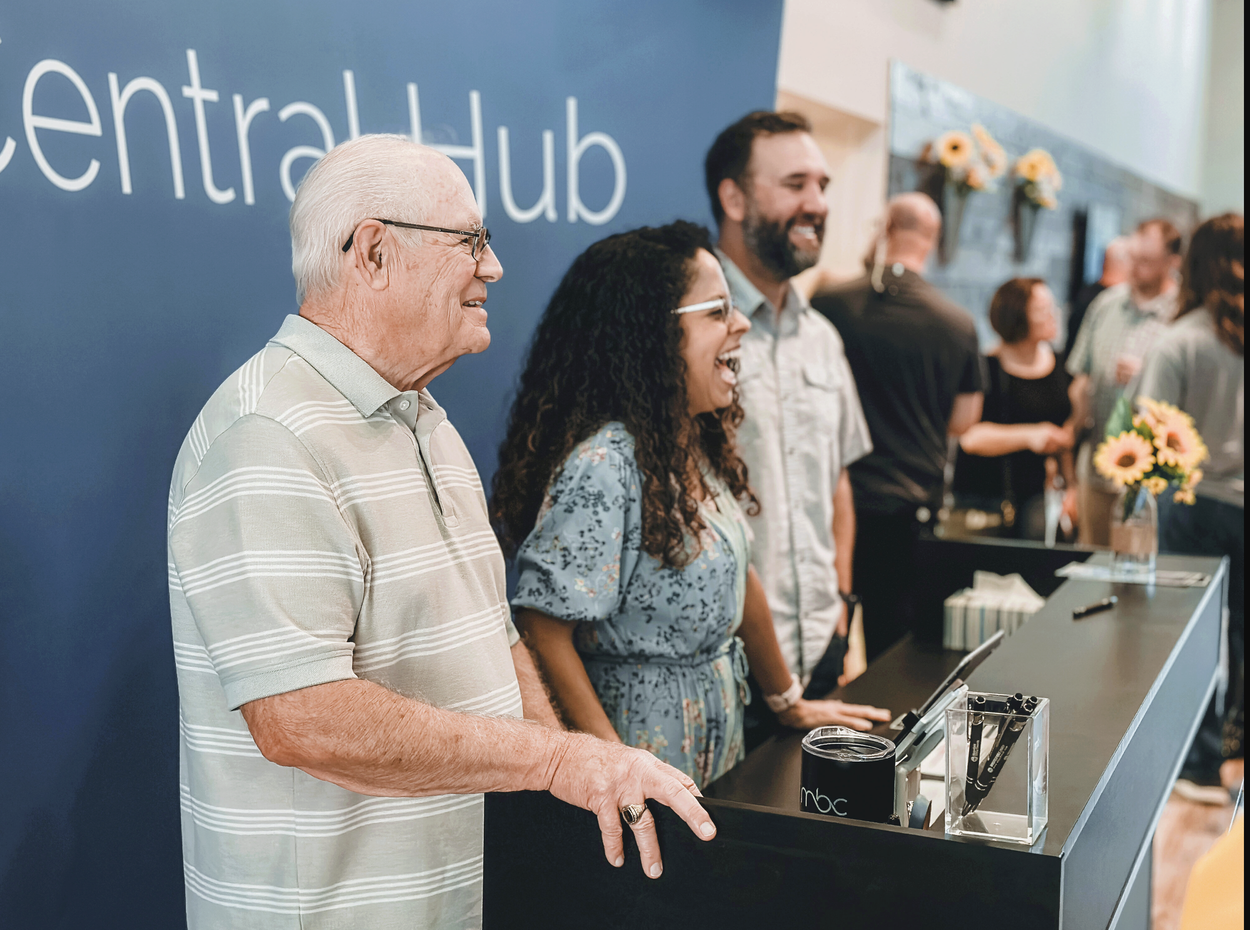 People at a reception desk in a healthcare or community center, smiling and interacting.