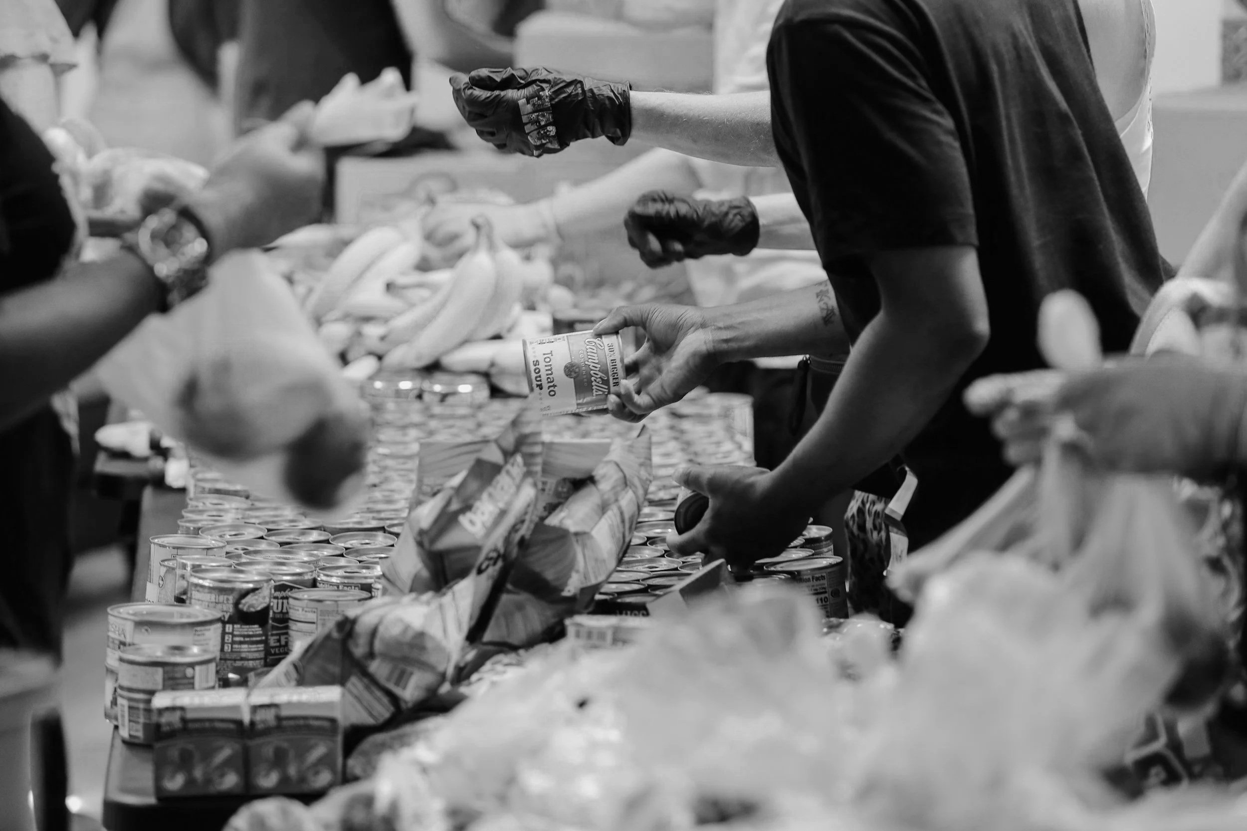 People distributing canned goods and food items on a table at a food drive or distribution event.