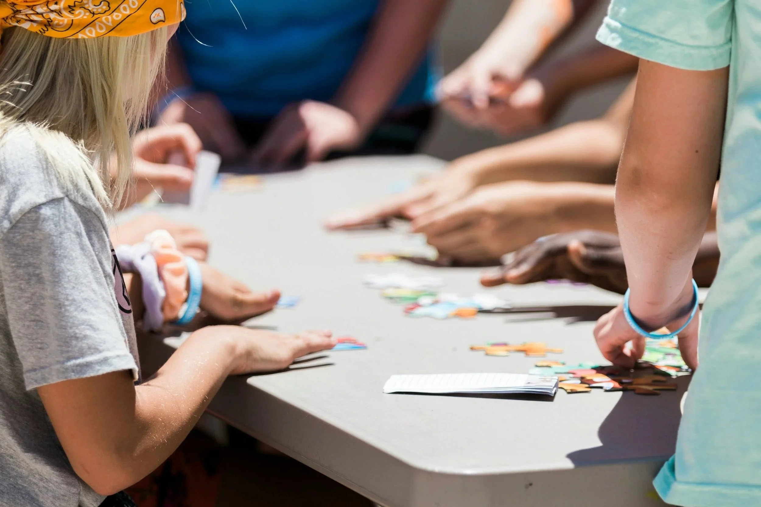 Children gathered around a table playing a card game outdoors.
