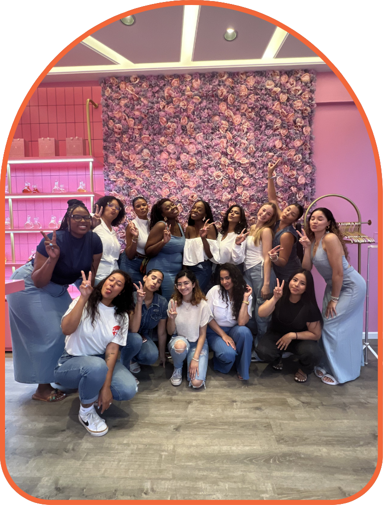 A group of women posing in front of a pink and purple floral wall inside a decorated room.