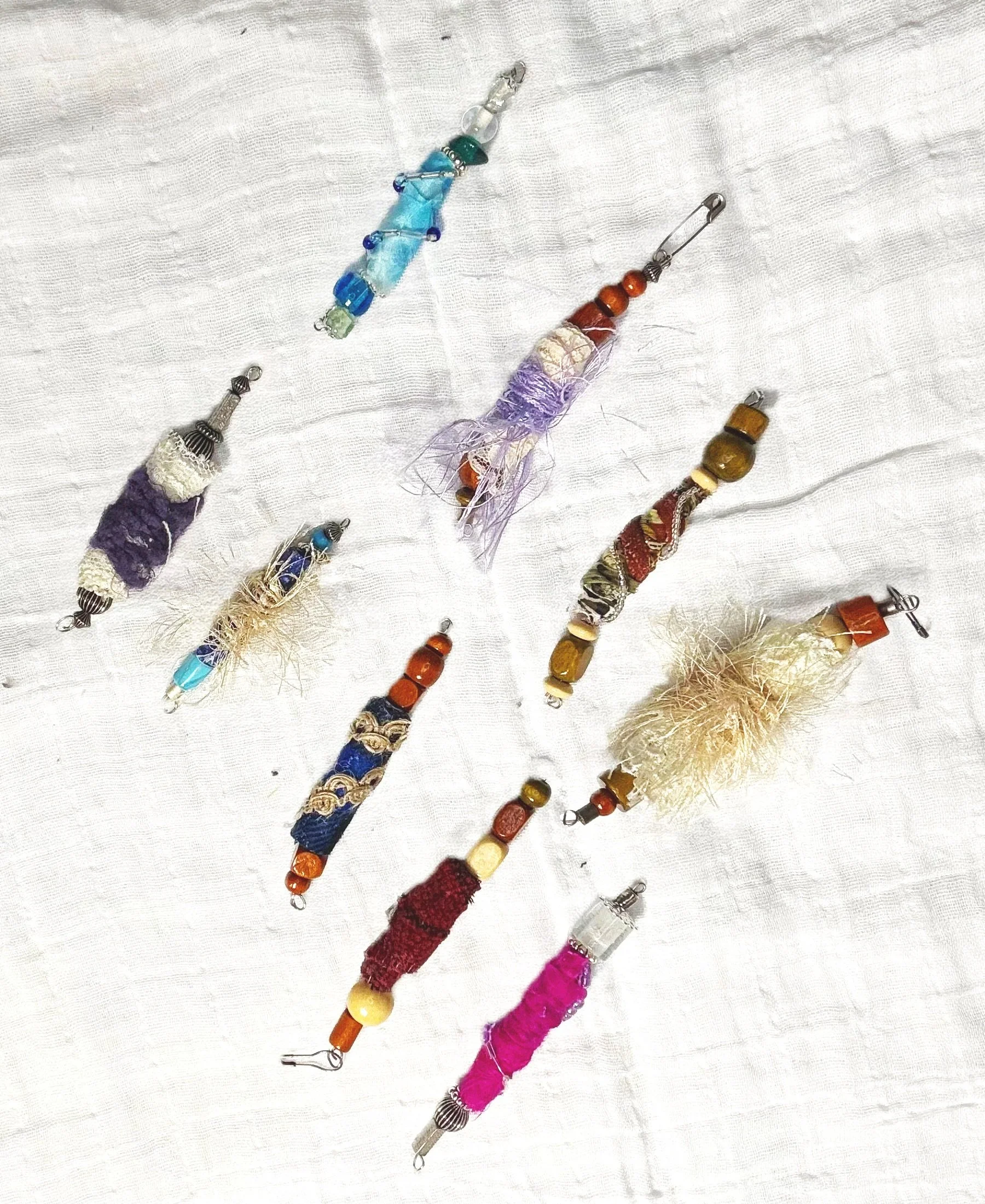 Assorted handmade beaded and fabric jewelry pieces with various colors, textures, and designs laid out on a white fabric background.