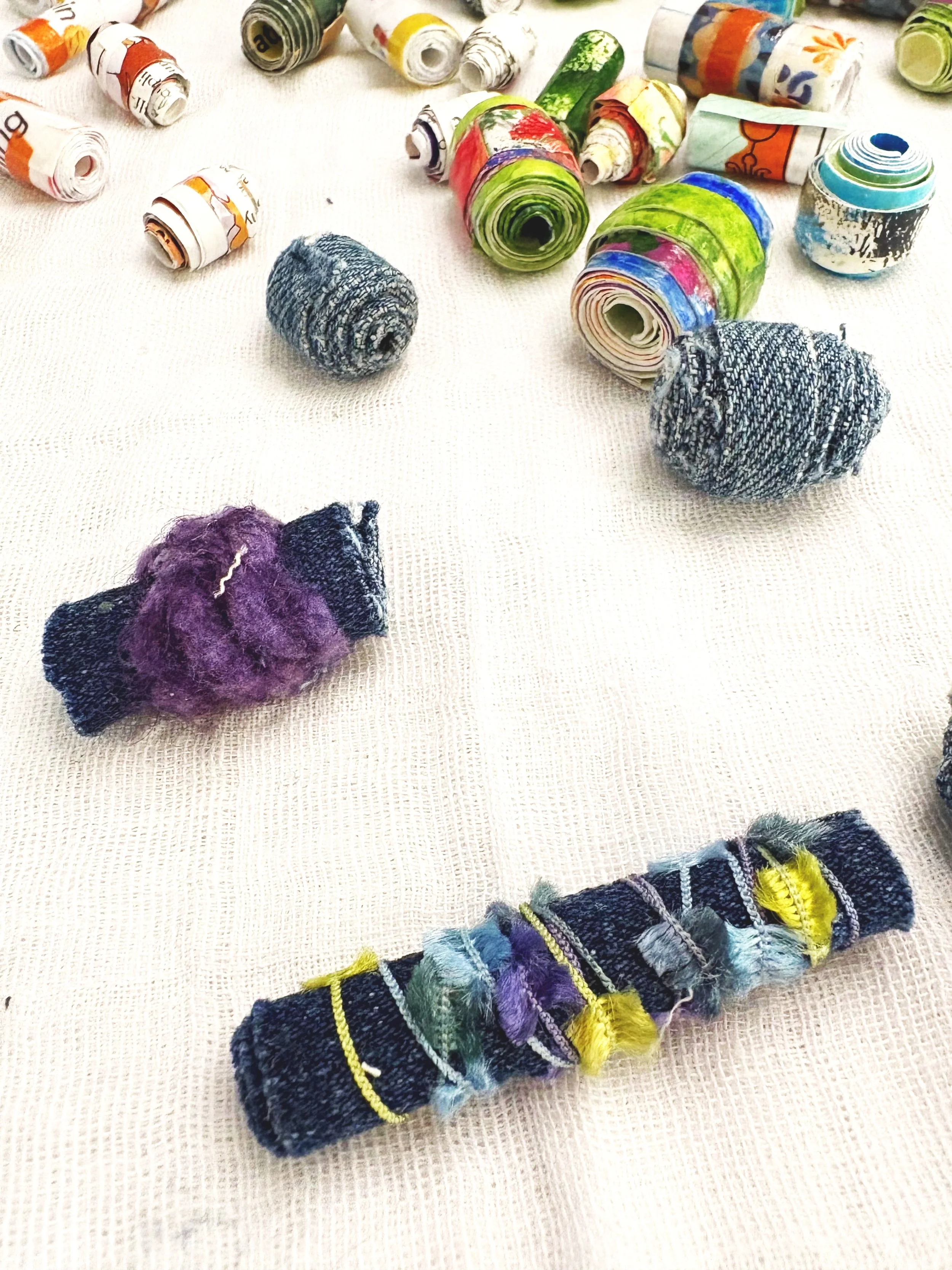 Colorful rolled-up paper with vibrant and patterned designs along with fabric or yarn balls on a beig textured surface.