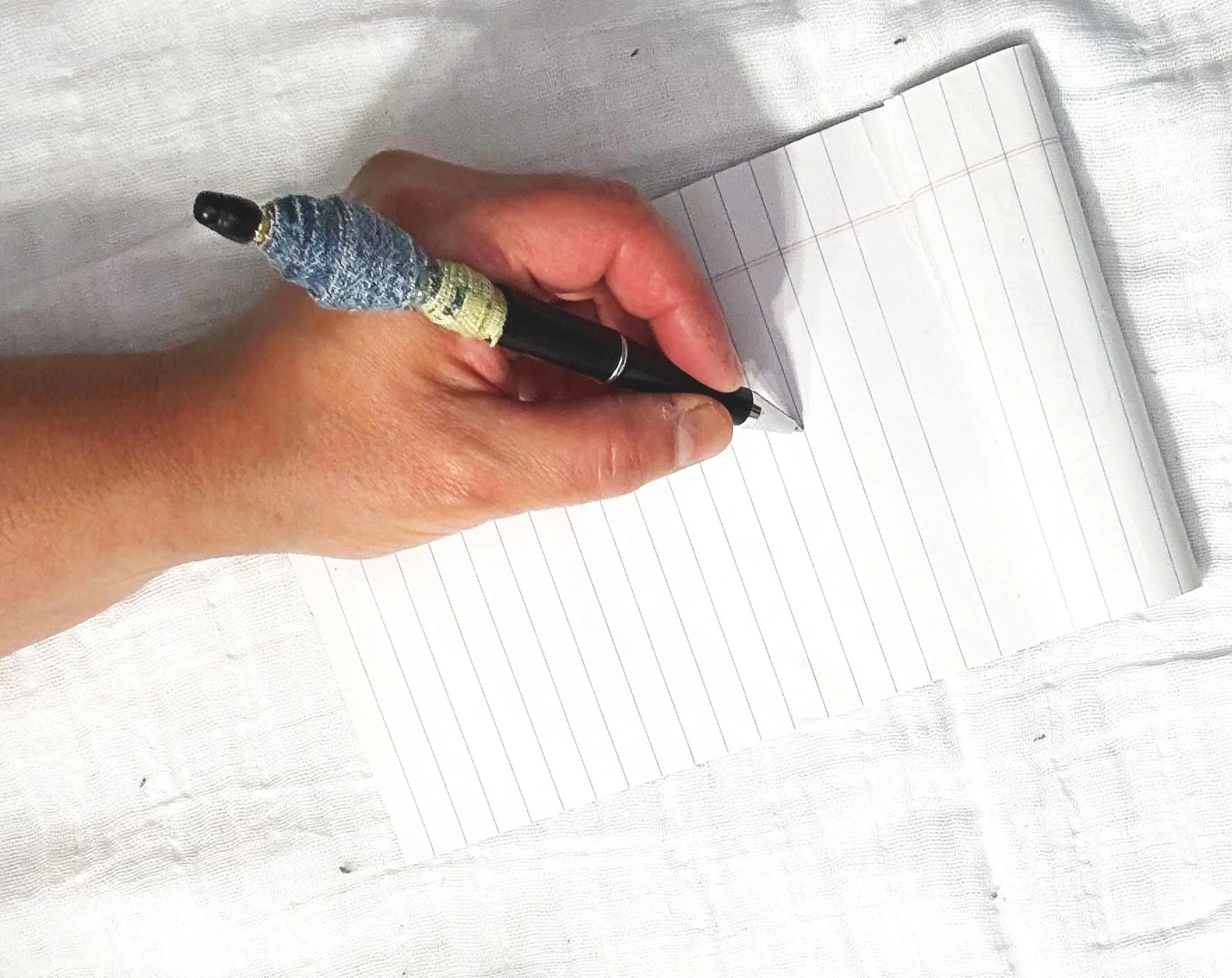 Close-up of a hand writing on lined notebook paper with a black pen wrapped in decorative foil.