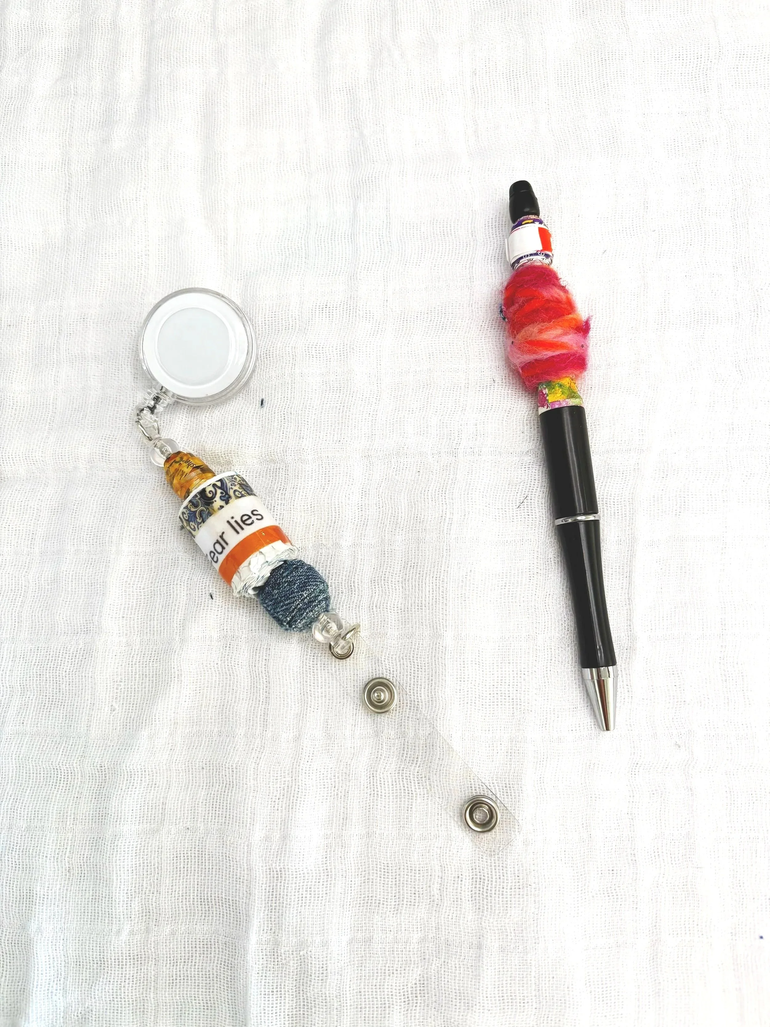 A black ballpoint pen with a colorful, fuzzy, pink, orange, and yellow decorative cover on a white textured surface, with two silver magnetic parts near the bottom.