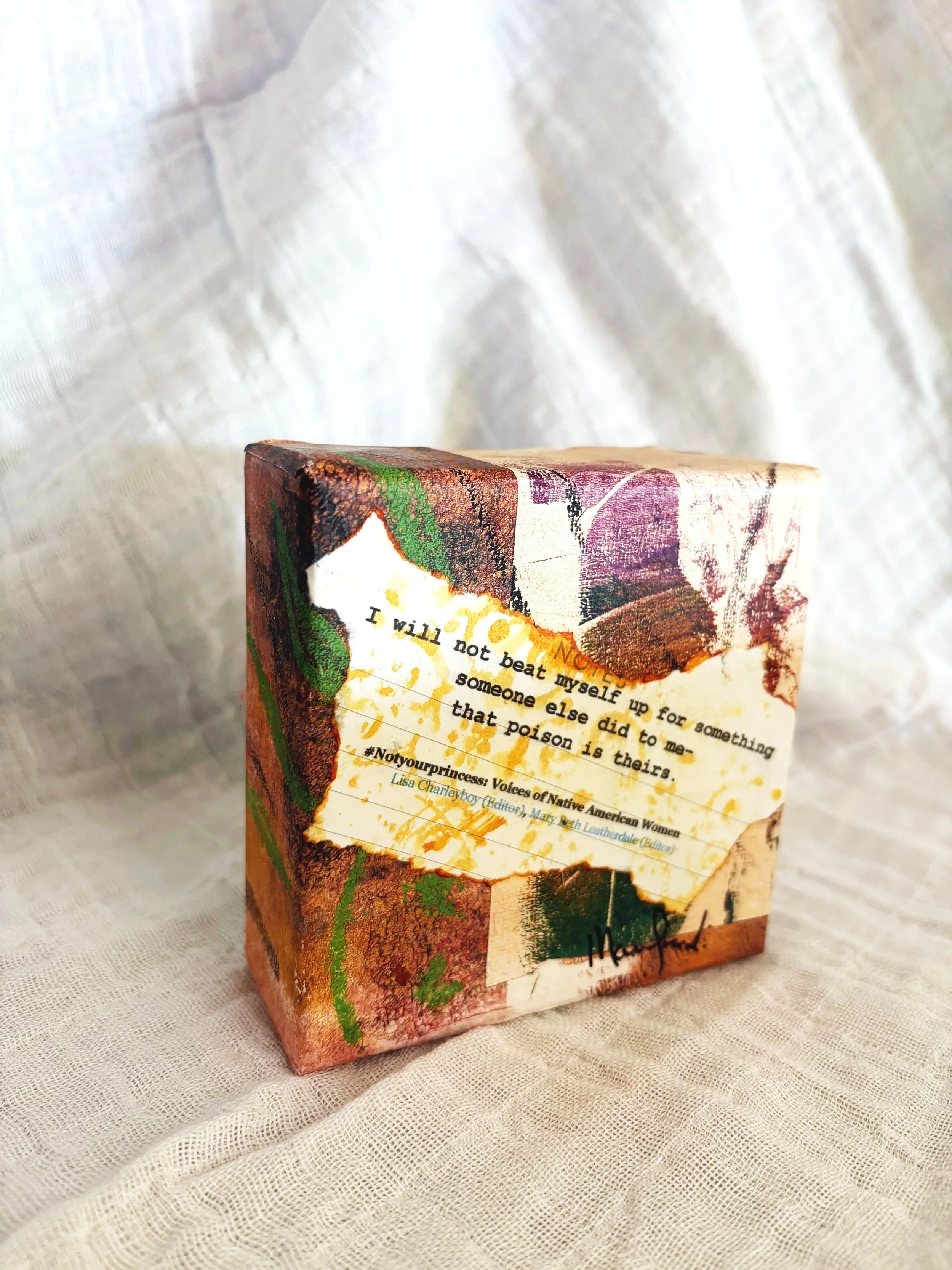 A close-up of a decorative book cover with artwork and text, sitting on a light-colored fabric surface.