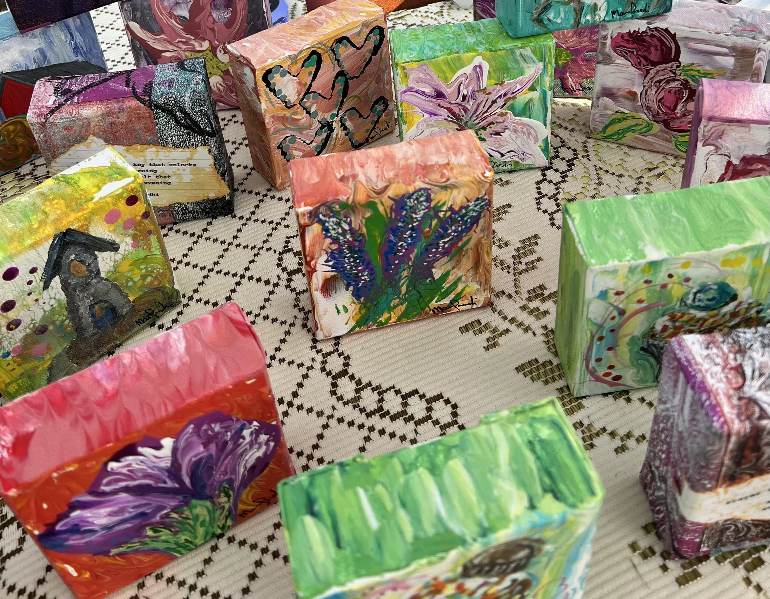 Small colorful abstract paintings displayed on a checkered surface.