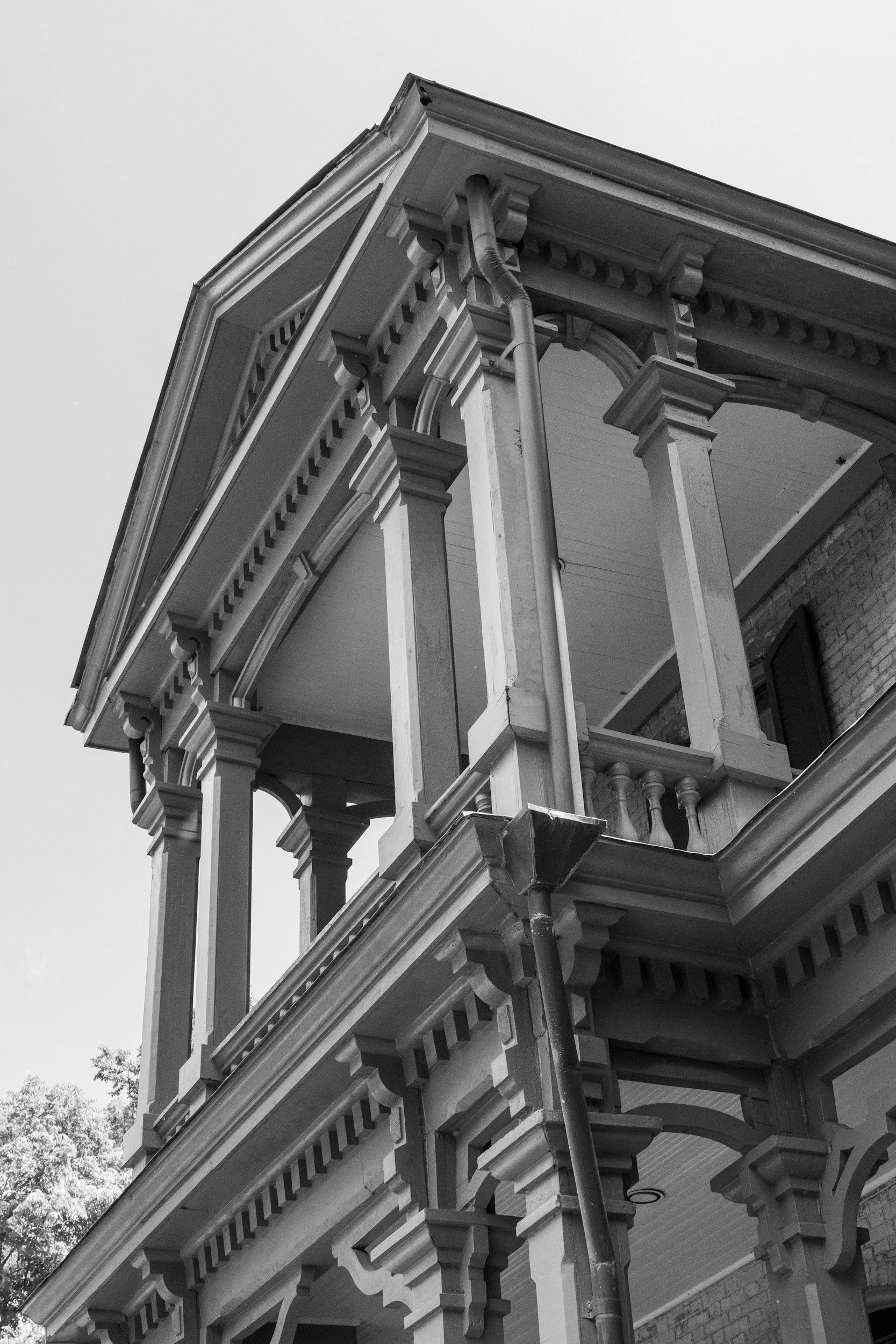 Black and white photo of a historic building with ornate architectural details, including decorative brackets, columns, and a pitched roof with a gutter system.