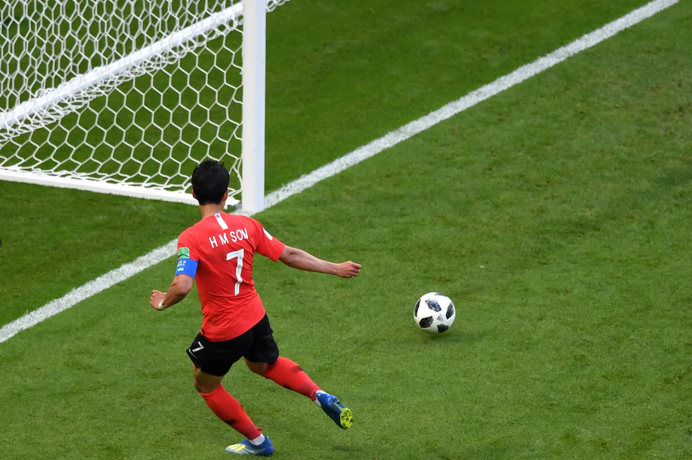 Soccer player in red jersey with the number 7, running towards the goal, preparing to kick the ball.