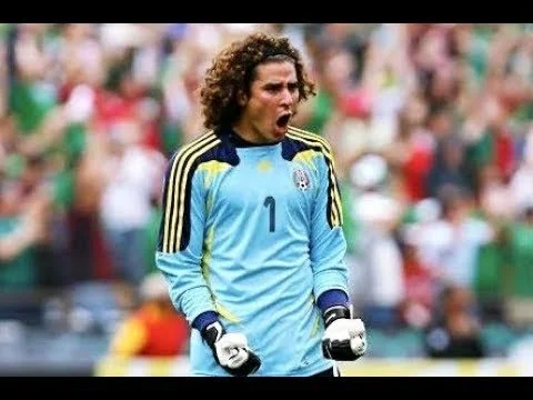 soccer goalkeeper celebrating on the field during a match, wearing a light blue jersey with the number 1, and standing amidst a crowd of spectators.