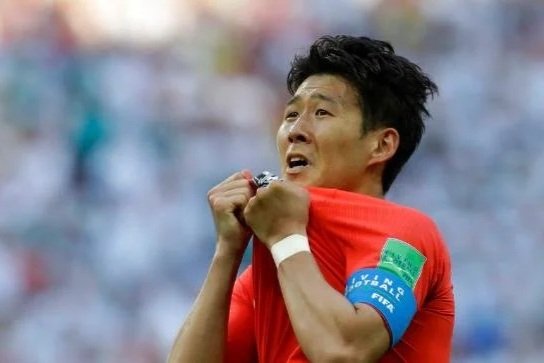 A soccer player wearing a red jersey and captain's armband celebrating on the field.