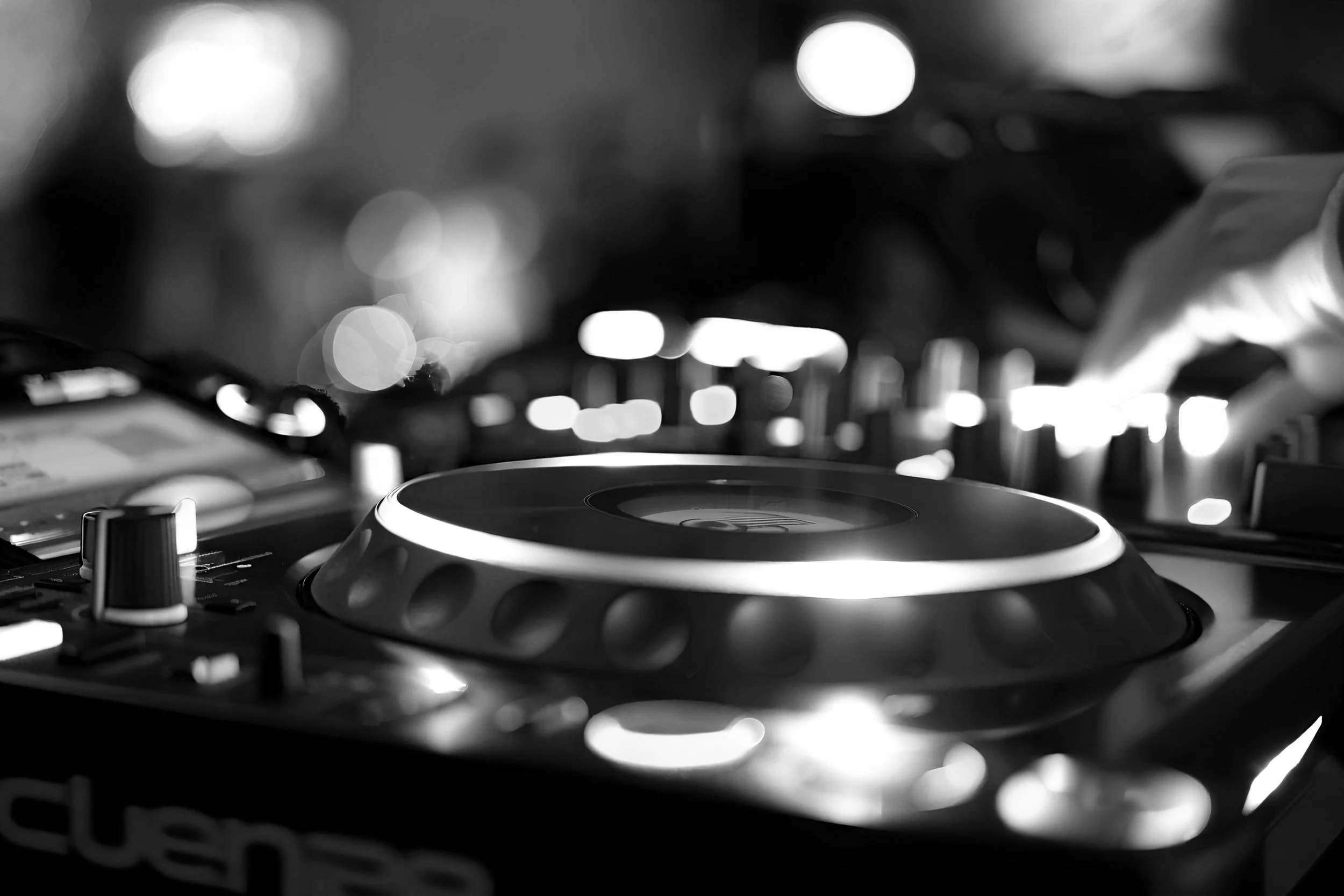 DJ mixer equipment with turntable in a dimly lit nightclub or event space, with blurred lights in the background.