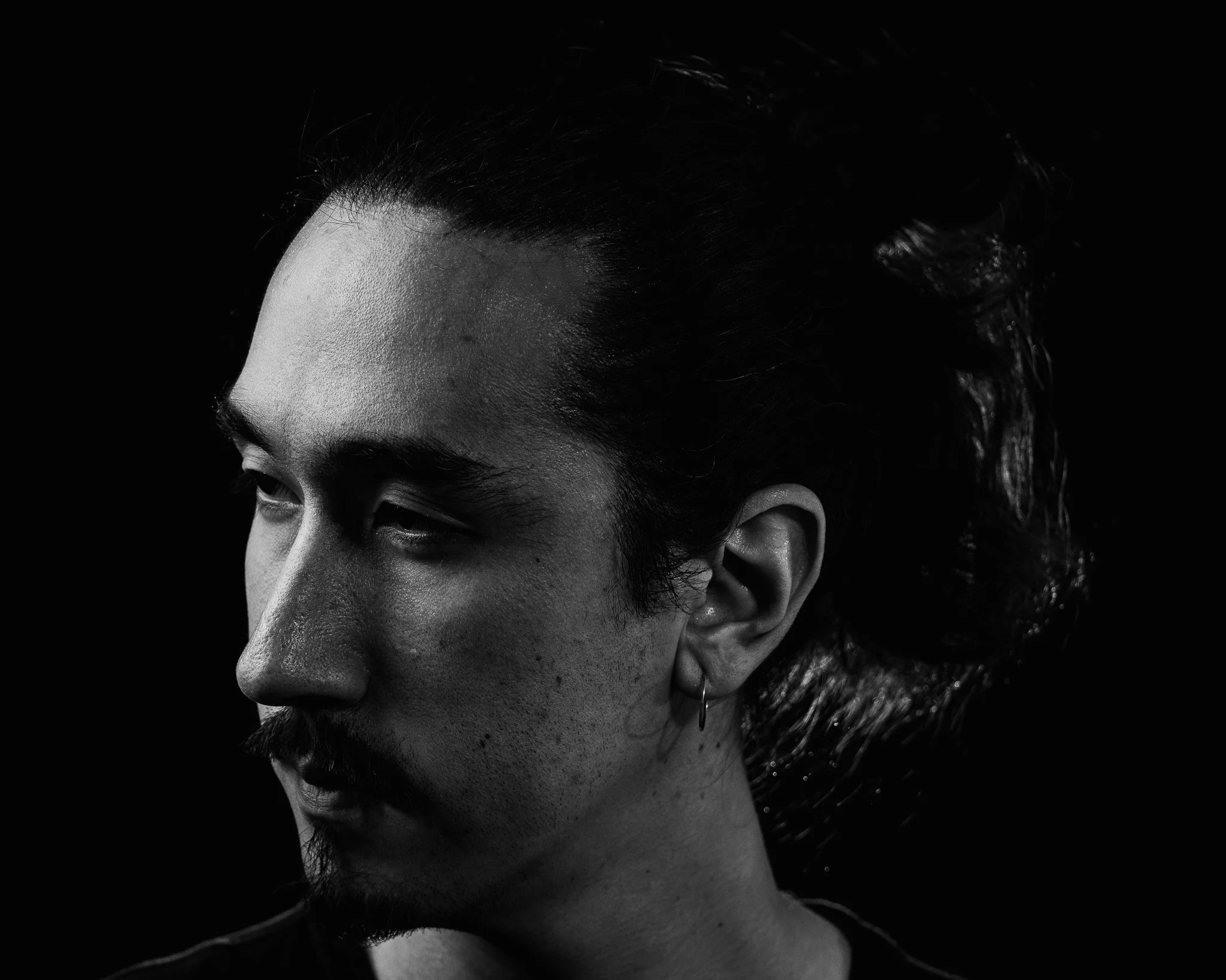 Black and white close-up photo of a person's face showing forehead, eye, eyebrow, nose, cheek, ear, and dark hair.