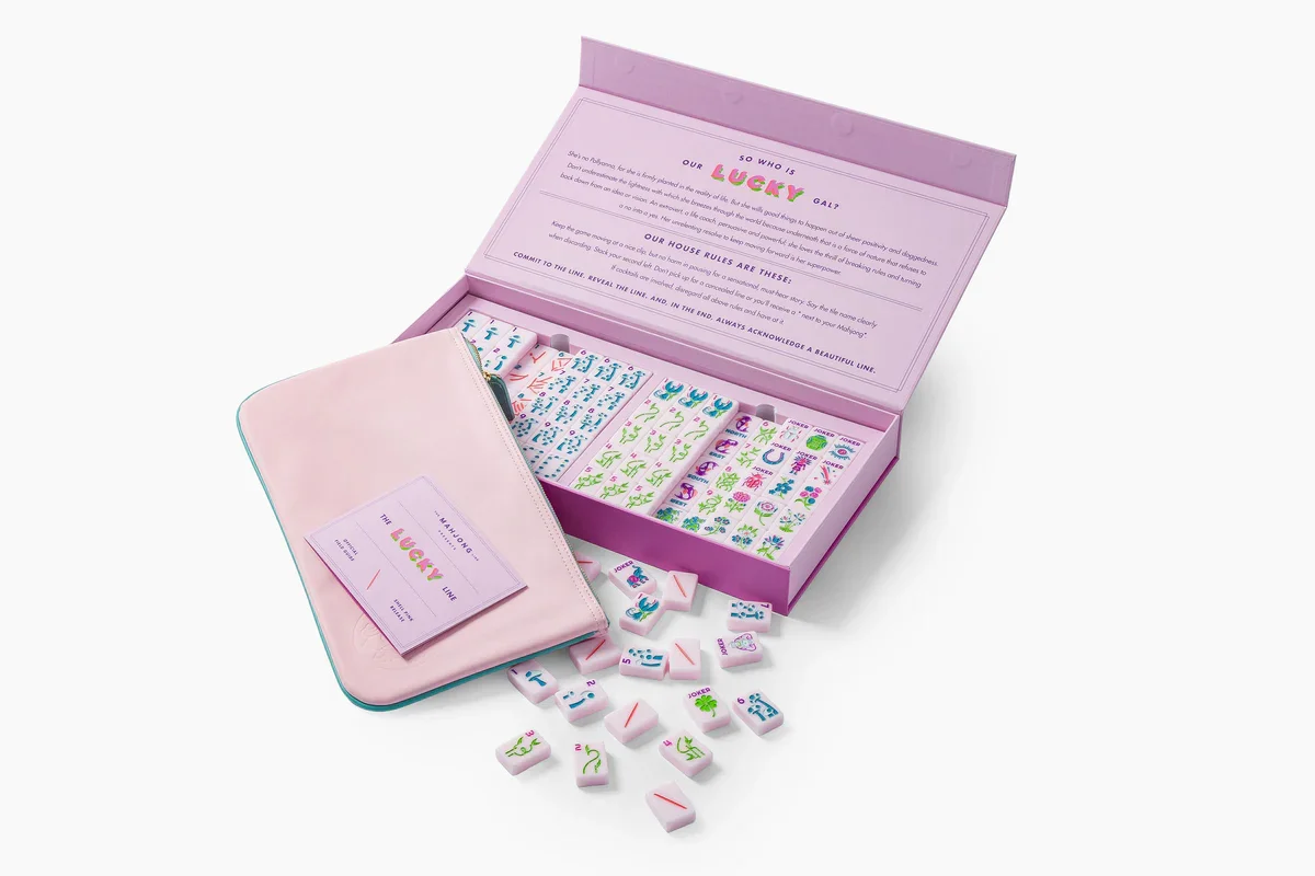 A pink box of Mahjong tiles with colorful designs and symbols inside, with some Mahjong tiles spilled out on a white surface.