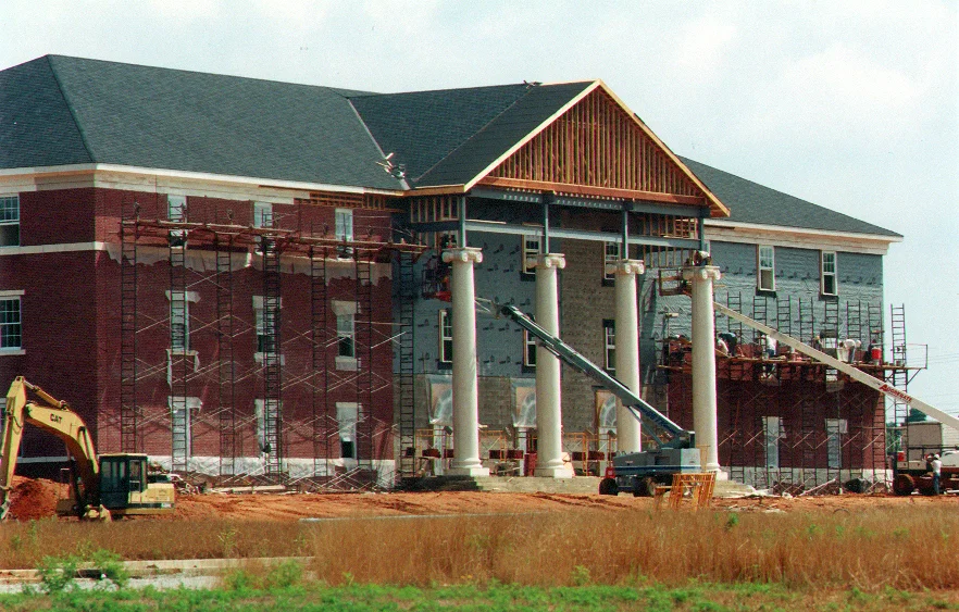 Under construction building with large columns and scaffolding, a construction vehicle is visible on the site.