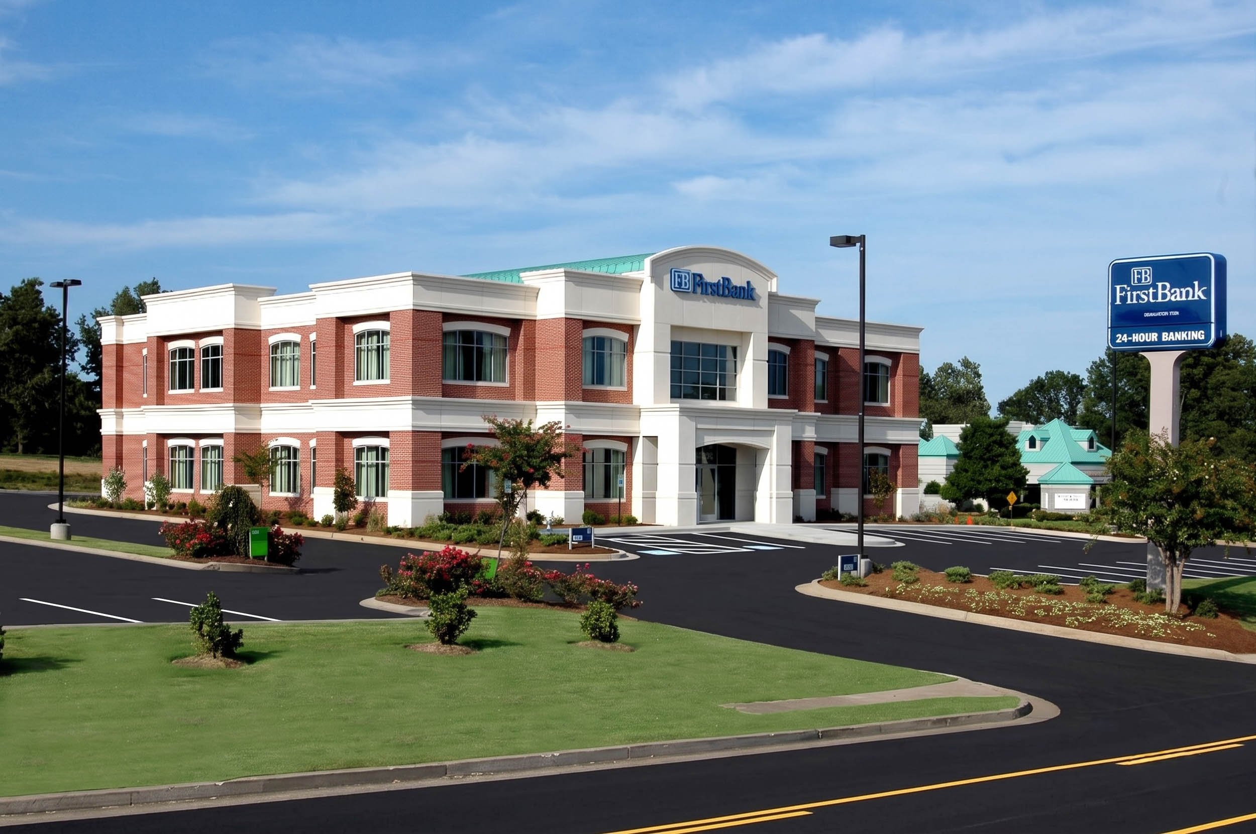 A modern brick and white building with a sign reading FirstBank, located in a parking lot with landscaped greenery and a clear blue sky.