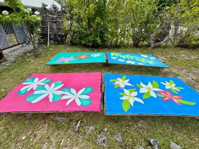 Four colorful towels with floral patterns are spread on the grass in a backyard with trees and bushes in the background.