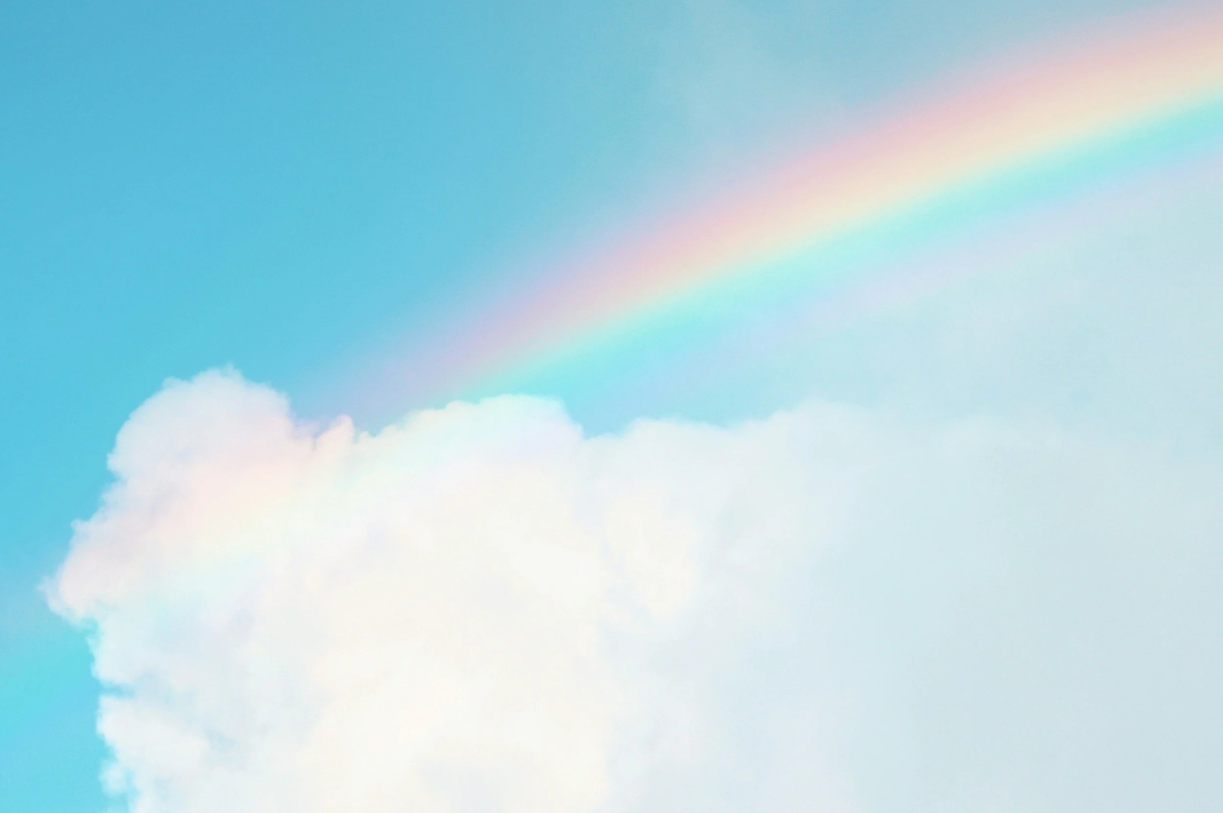 A sky with a faint rainbow and some white clouds.