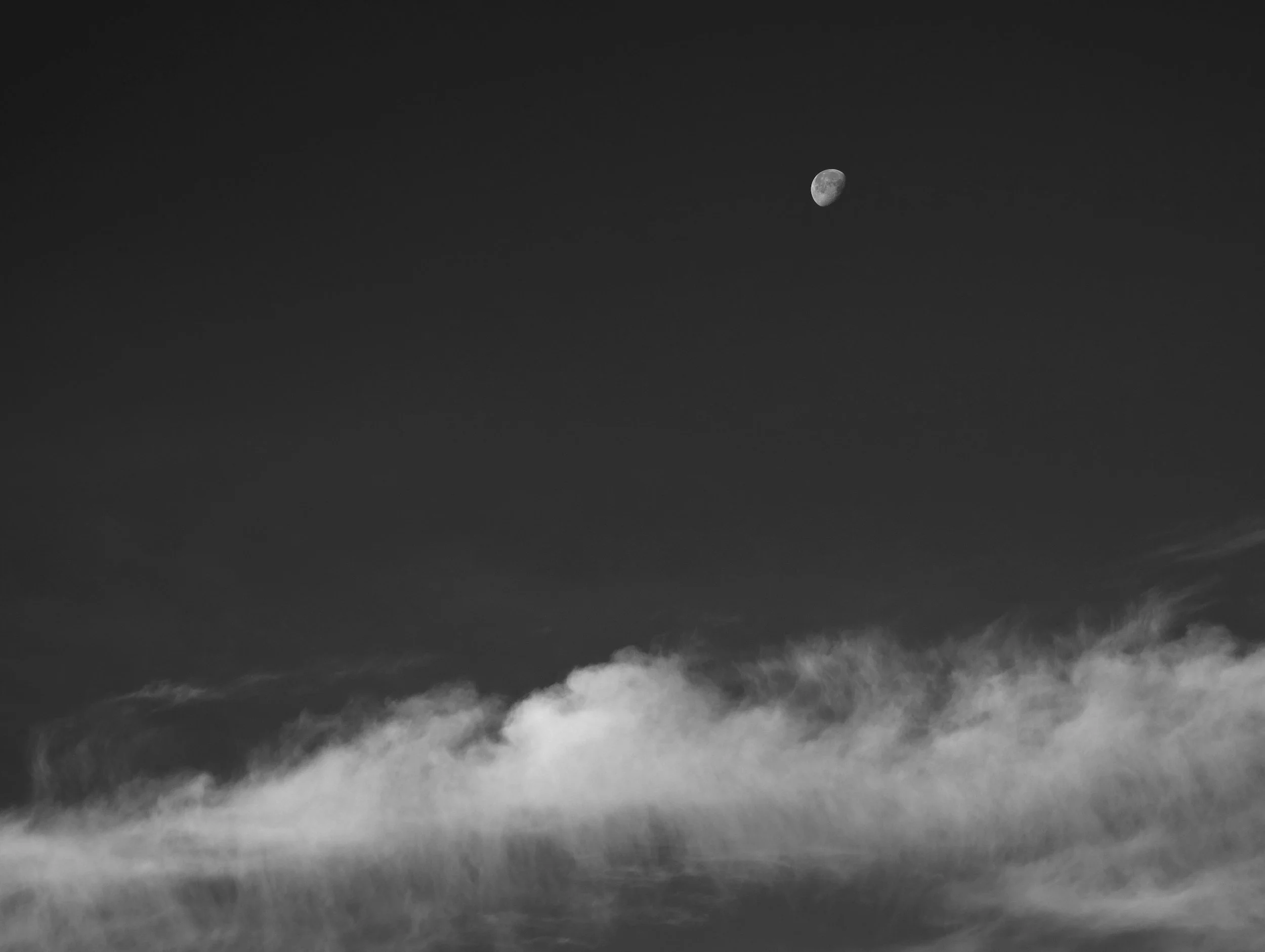 Black and white photograph of the moon visible in the night sky above clouds.