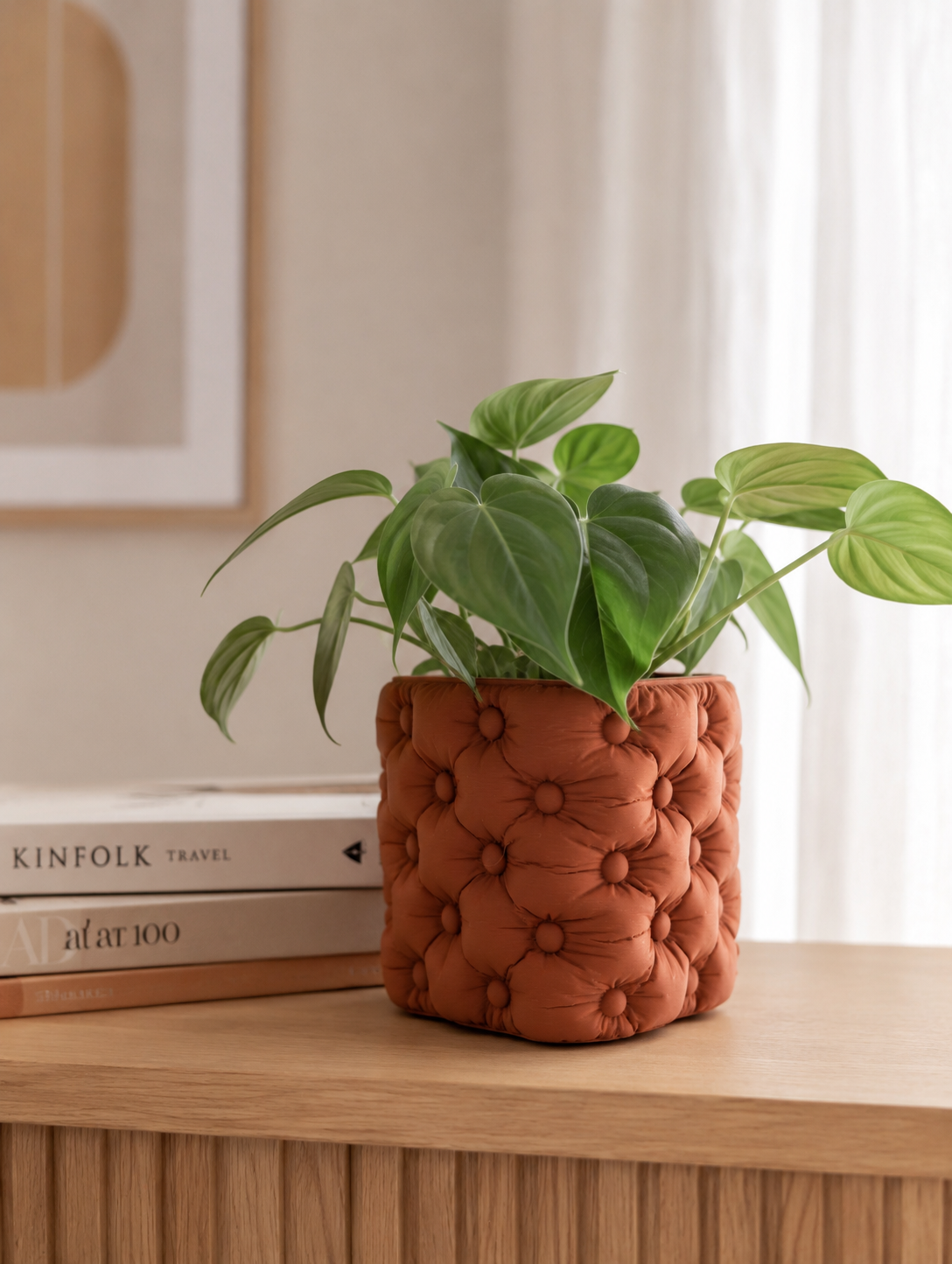 Een groene kamerplant in een pot van oranjebruine stof met reliëf die 3D geprint is, op een houten ondergrond met boeken op de achtergrond.