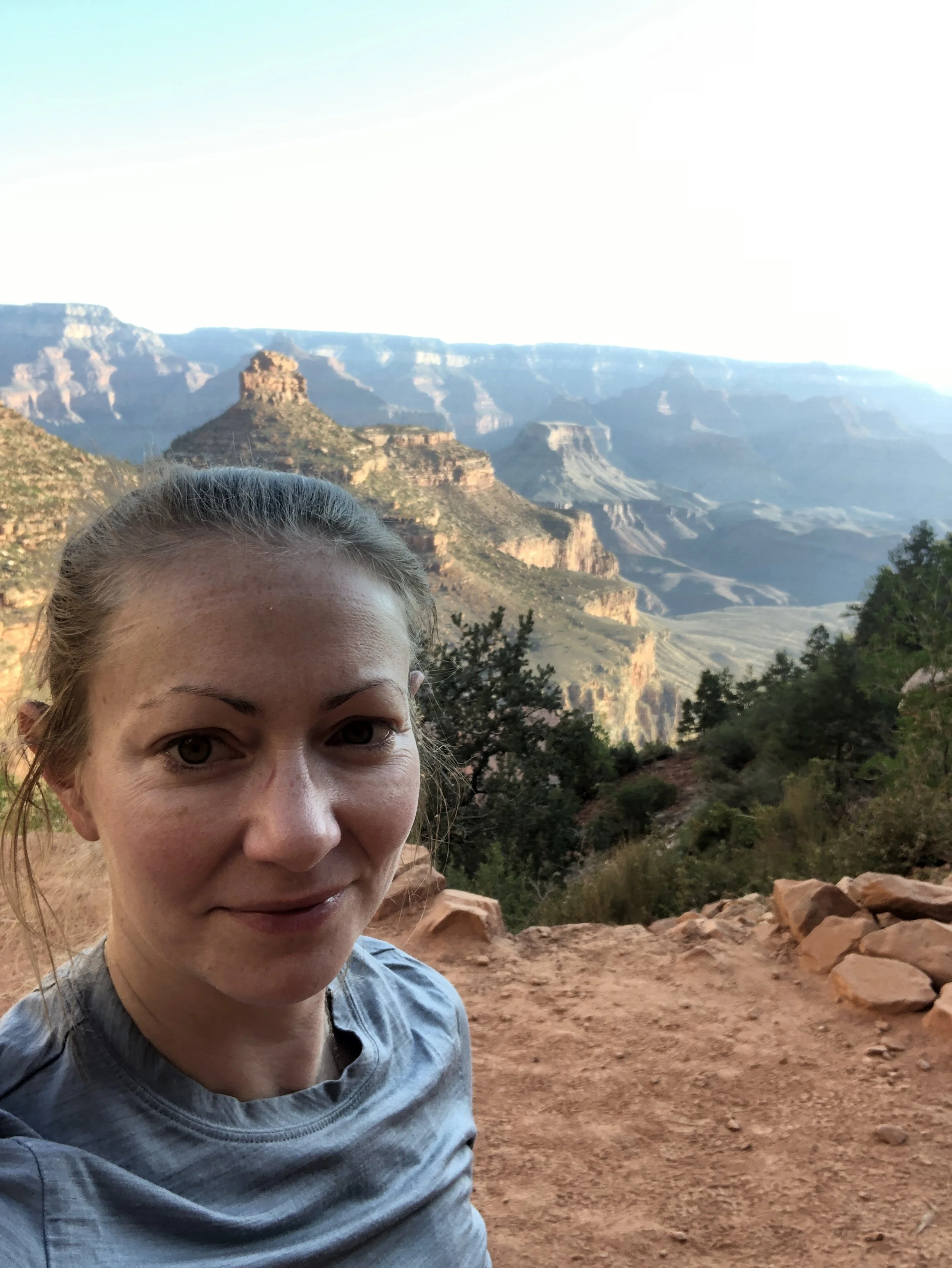 A woman taking a selfie at the Grand Canyon, with canyon cliffs and rock formations in the background.