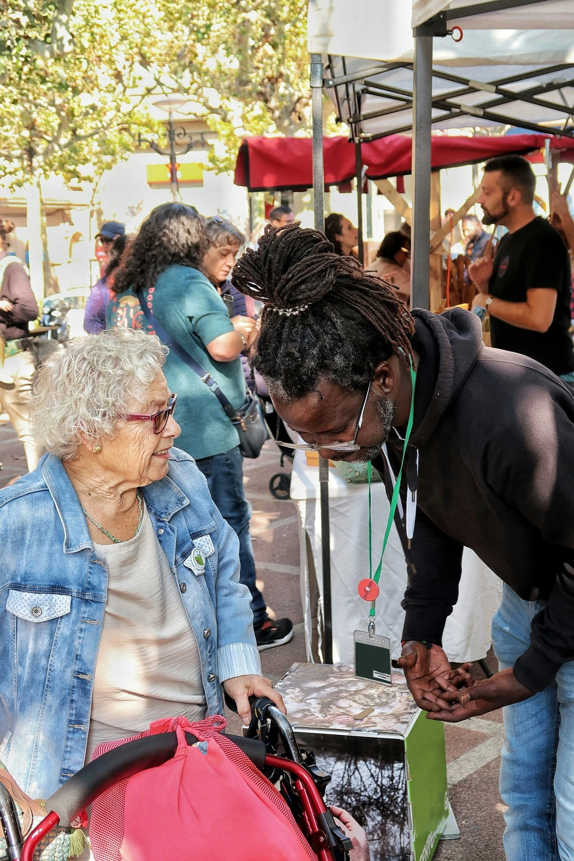 A diverse group of people gathered at an outdoor event, engaging in conversations and activities under tents, with trees visible in the background.