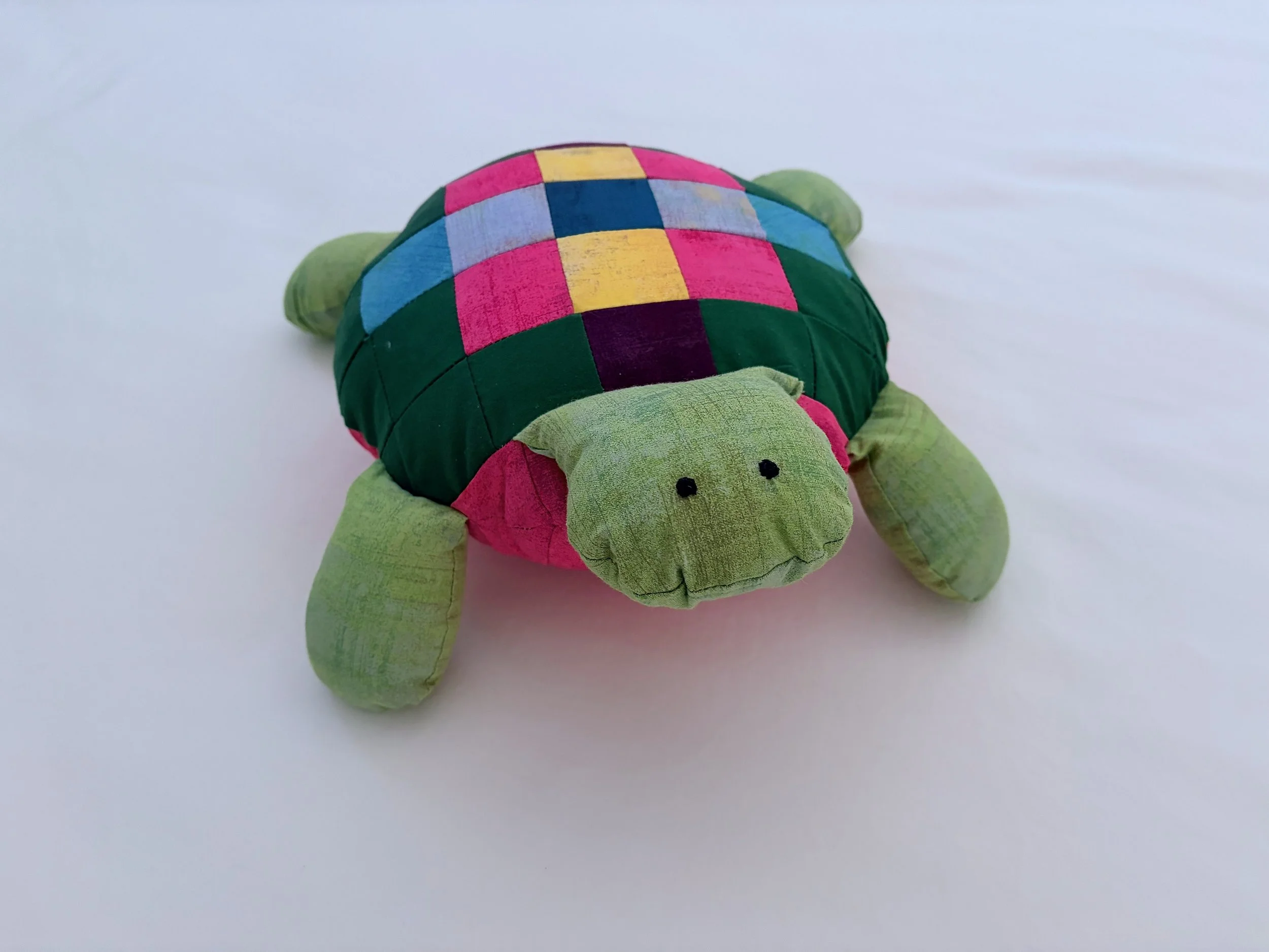 Colorful plush turtle toy with a checkered shell on a white background.