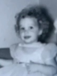 Child with curly hair smiling and sitting at a table, black and white photo.
