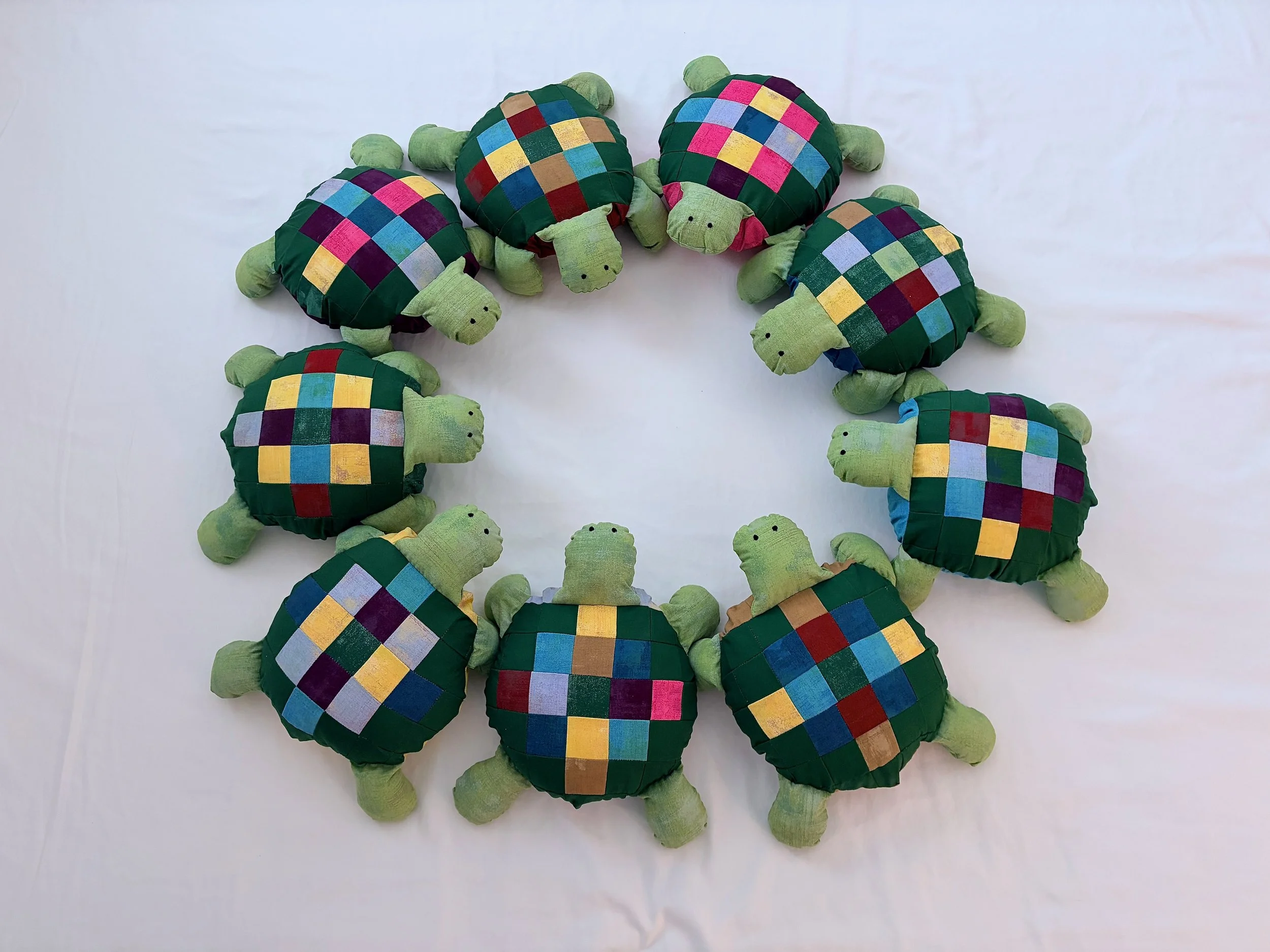 Five plush turtles with green bodies and patchwork shells in various colors, arranged on a white background.
